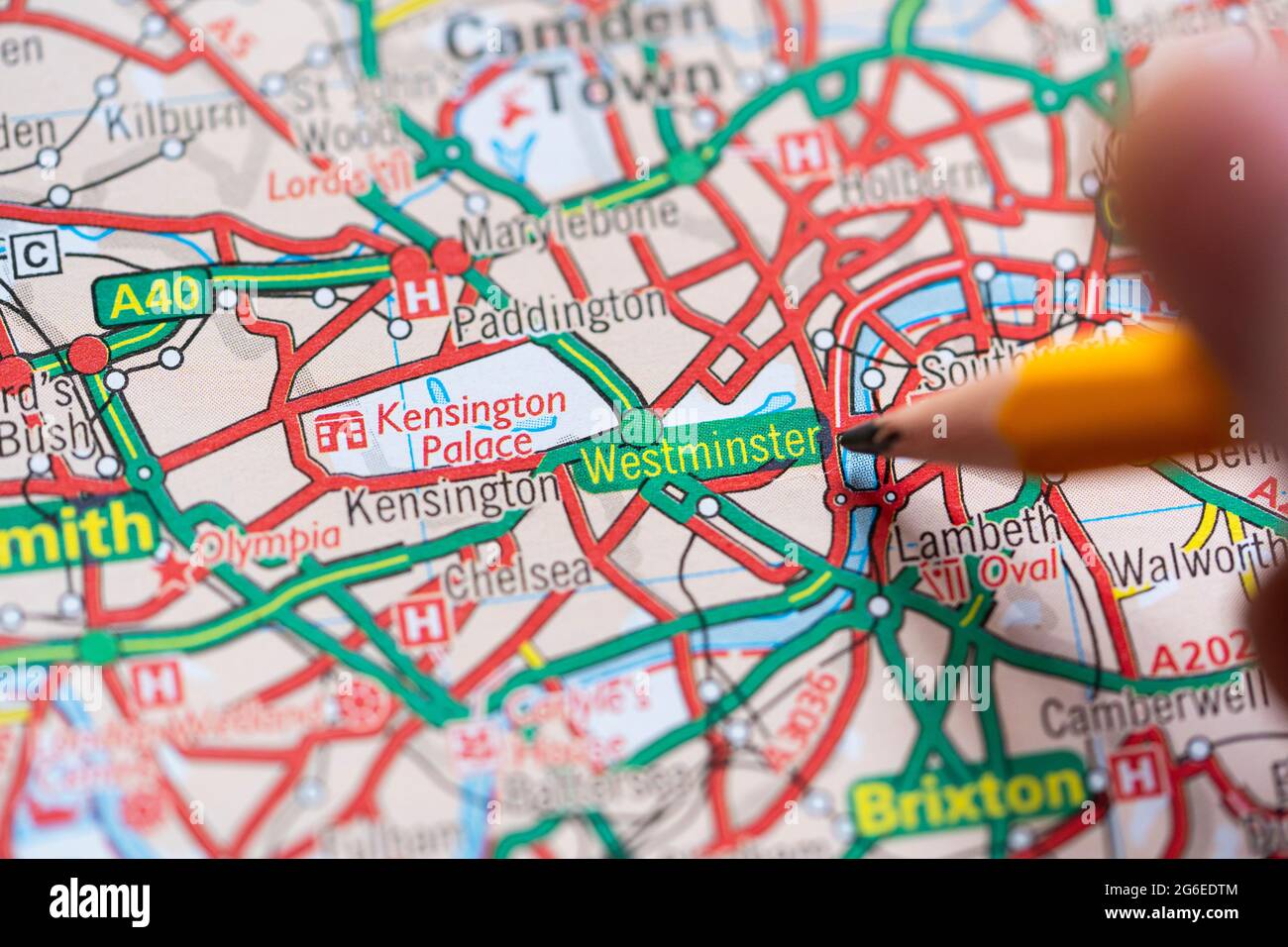 Nahaufnahme einer Seite in einem gedruckten Straßenkarte-Atlas mit einer Männerhand, die einen Bleistift hält, der auf den Stadtteil Westminster im Zentrum von London, England, zeigt Stockfoto