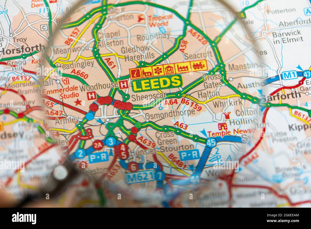 Makro-Nahaufnahme einer Seite in einem gedruckten Straßenkarte-Atlas mit einer Männerhand, die eine Lupe hält, die eine Vergrößerung der Stadt Leeds, England, zeigt Stockfoto