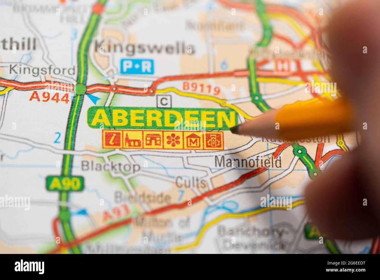 Eine Makroaufnahme einer Seite in einem gedruckten Roadmap-Atlas mit einer Männerhand, die einen Bleistift hält und auf die schottische Stadt Aberdeen zeigt Stockfoto