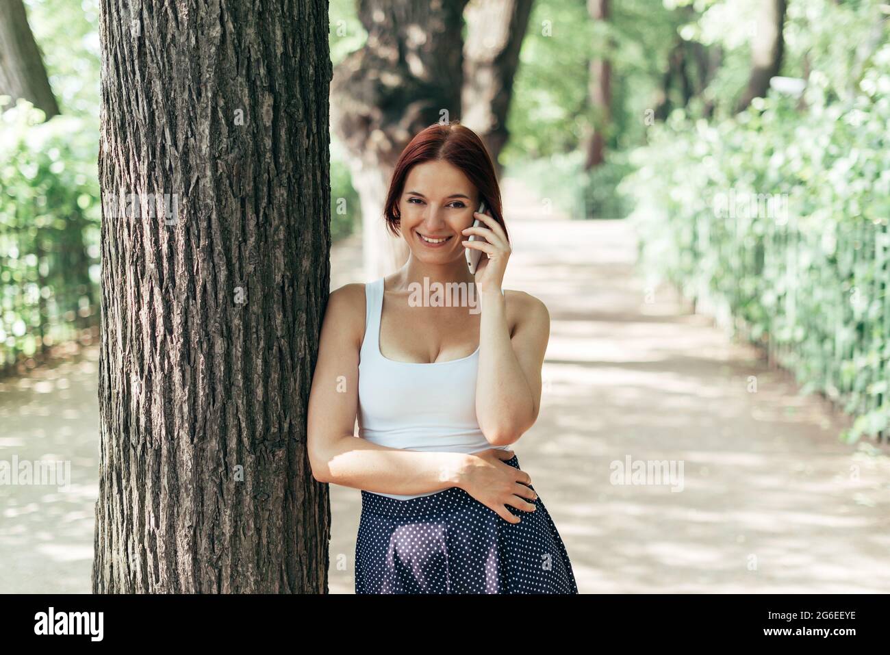 Mädchen lacht, während sie im Sommer auf einem Smartphone im Park spricht und Fernsehkameras gucken. Stockfoto