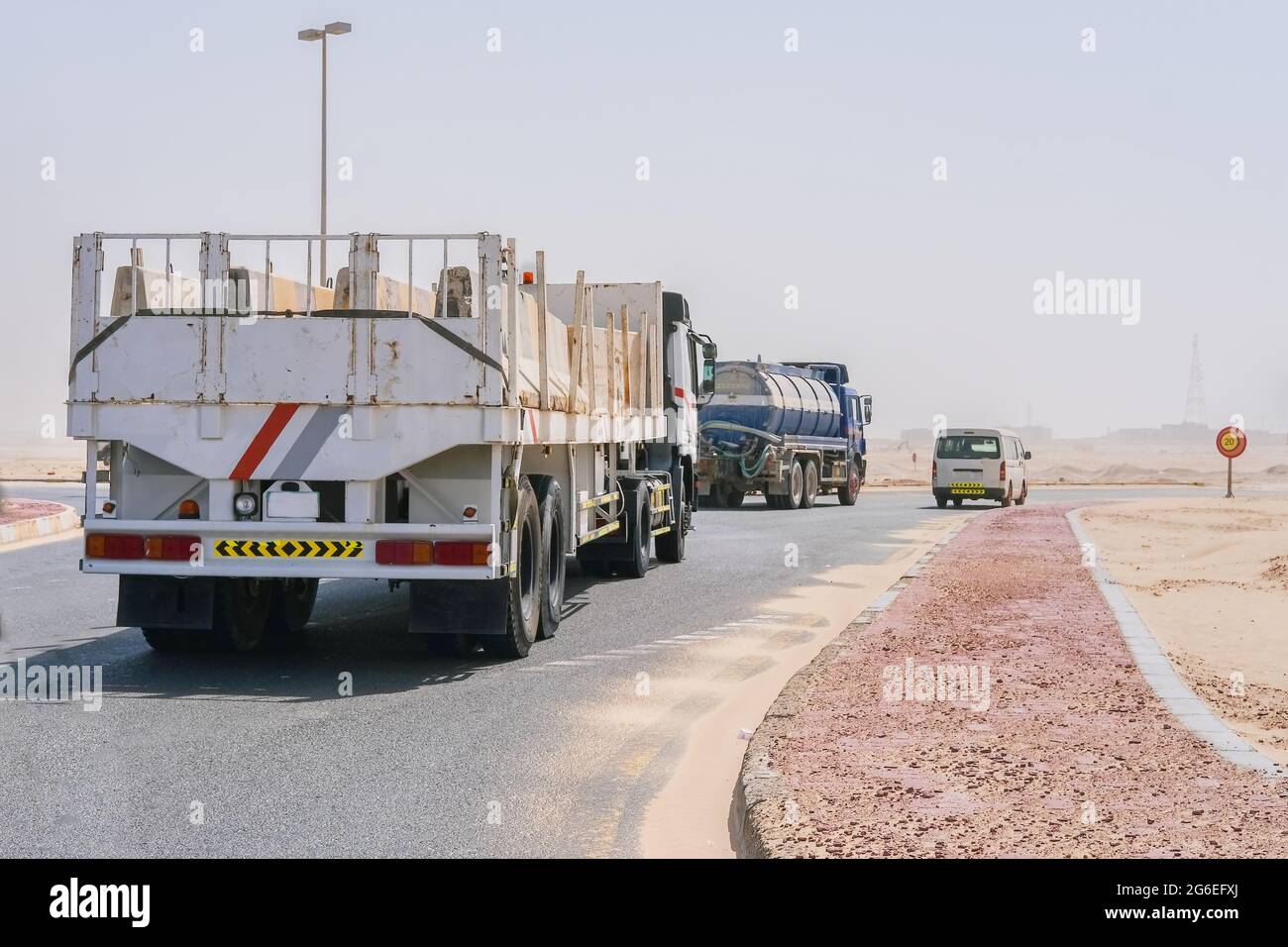 Gruppe von LKW-Transporten, Lieferwagen und Tankwagen, auf der Autobahn durch die Wüste mit verschwommenen Sanddünen im Hintergrund durch Sandsturm. Stockfoto