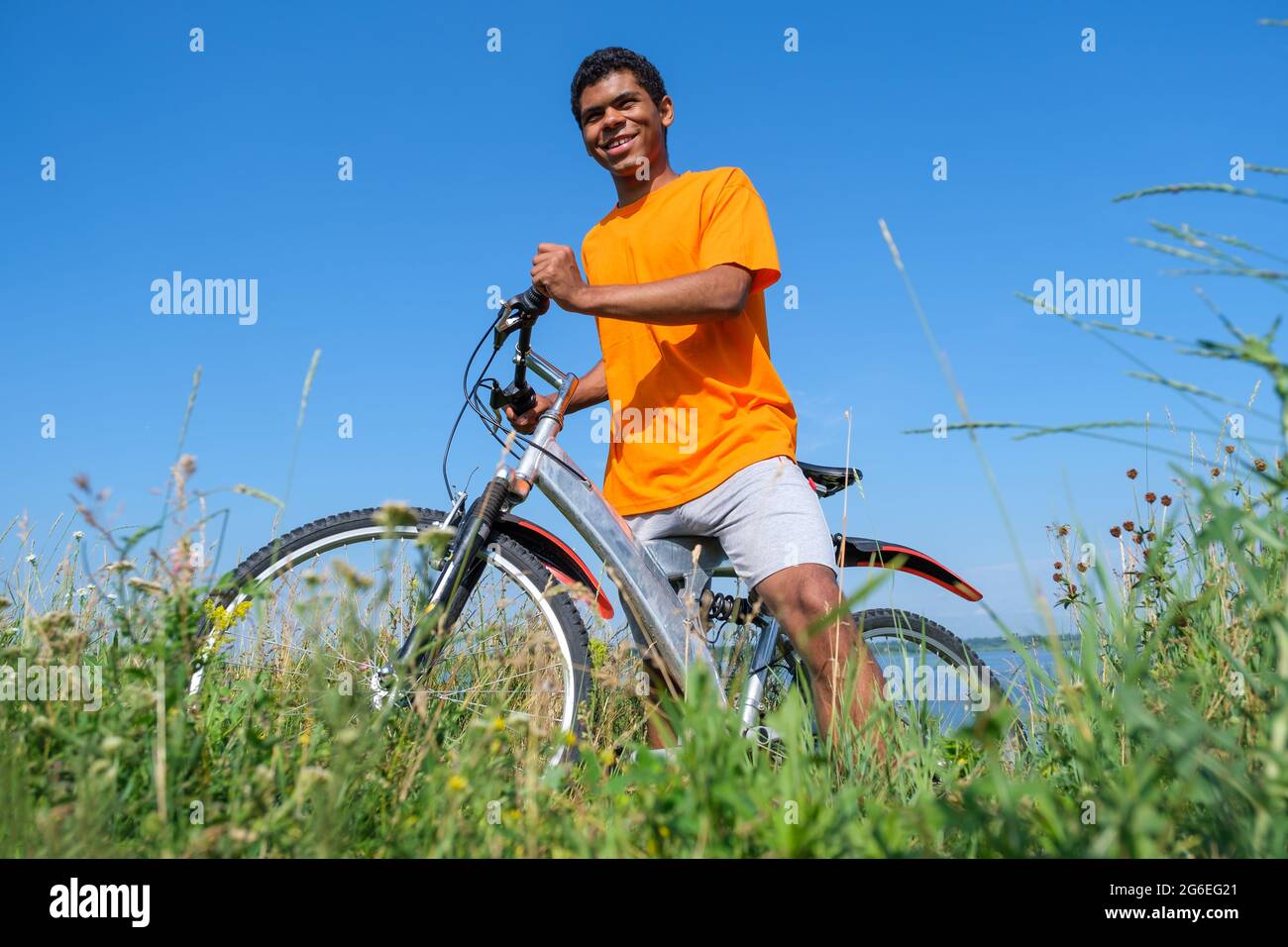 Afroamerikanischer Mann, der mit dem Fahrrad auf der Wiese gegen den blauen Himmel steht Stockfoto