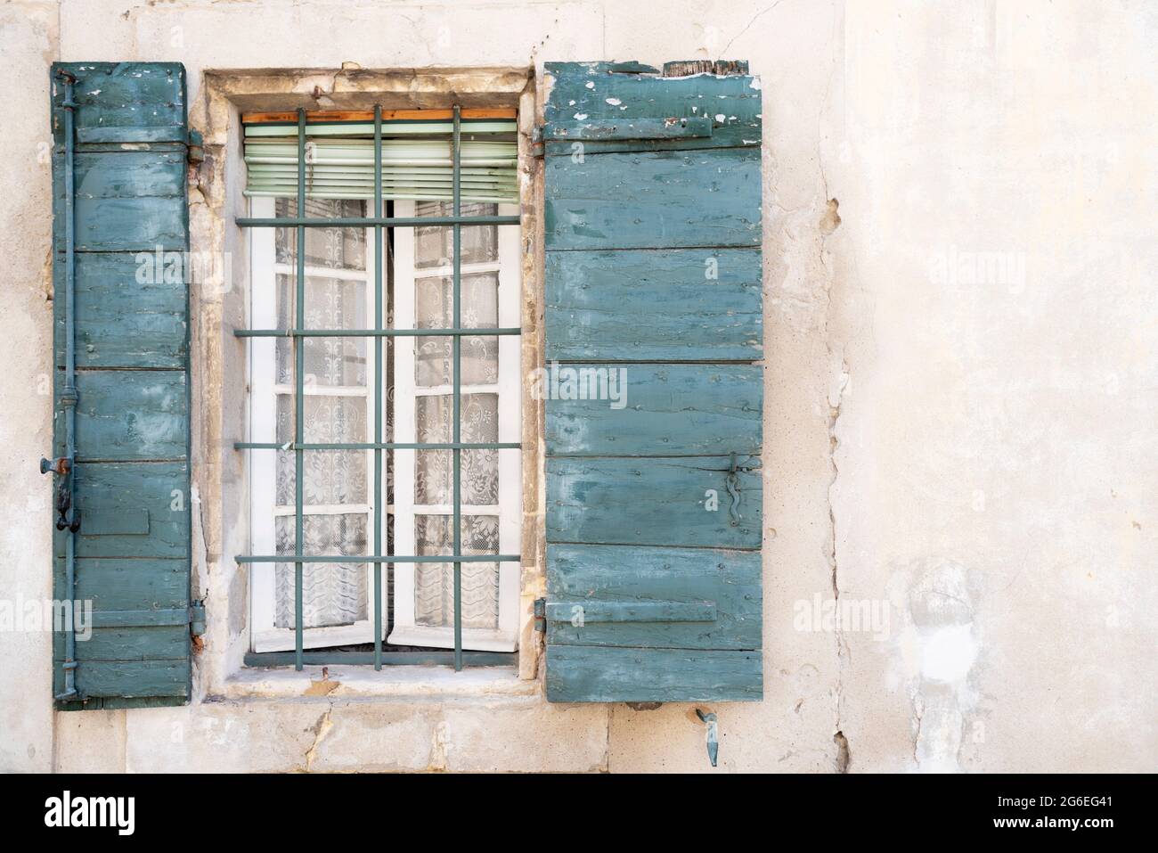 Alte Fassade mit Gitterfenster mit Vorhang und hölzernen Fensterläden. Stockfoto