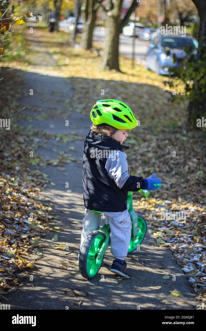 Kleinkind, das sein Push-Bike in einem grünen Helm reißt Stockfoto