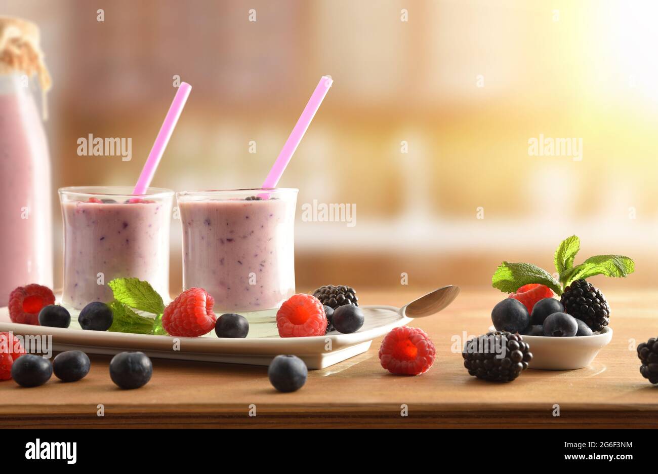 Waldfrucht-Smoothie mit Milch in Glasgläsern auf weißem Teller und Obst auf Holztisch in rustikaler Küche. Vorderansicht. Stockfoto