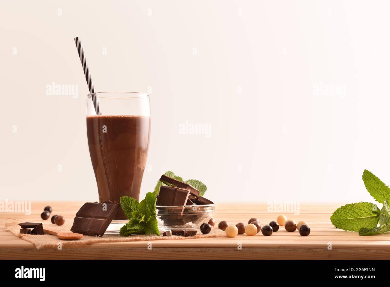 Glas mit Milchschokolade-Shake auf Holztisch mit Portionen Schokolade und Minzblättern mit isoliertem Hintergrund Stockfoto