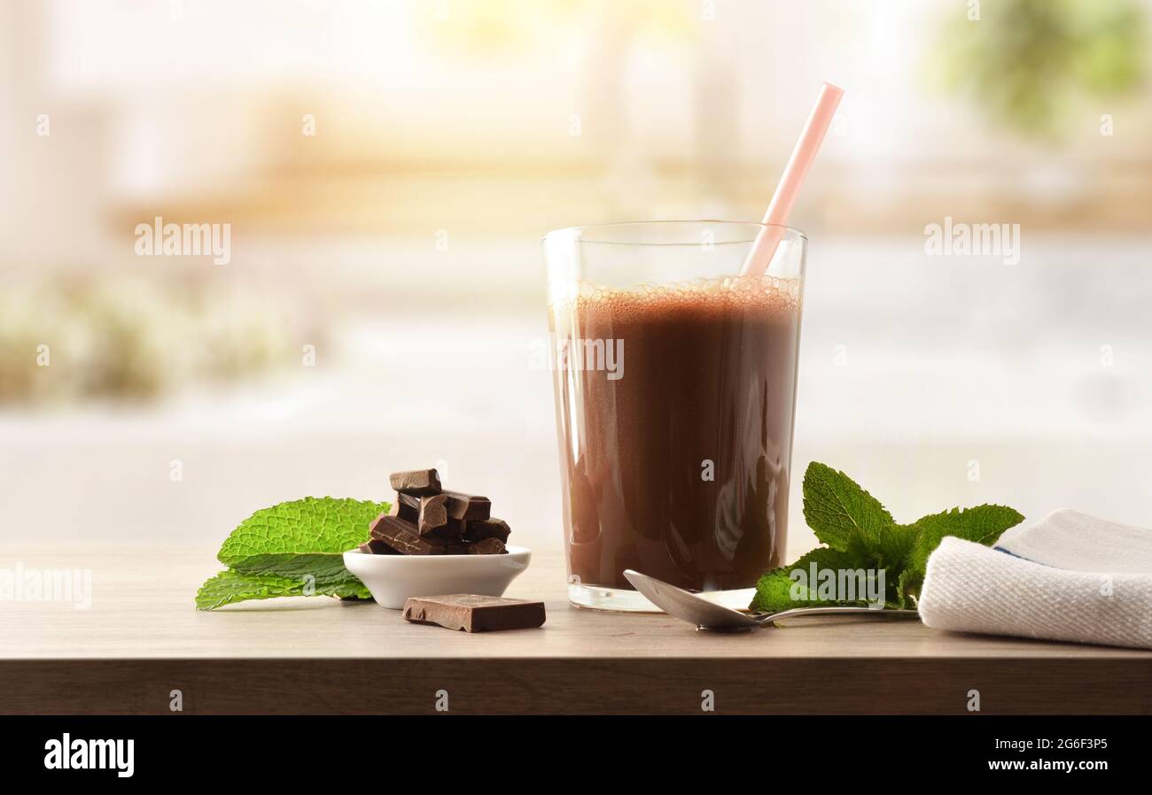 Glas mit Milchschokolade Shake mit Schokoladenportionen auf Holzbank in der Küche. Vorderansicht. Stockfoto