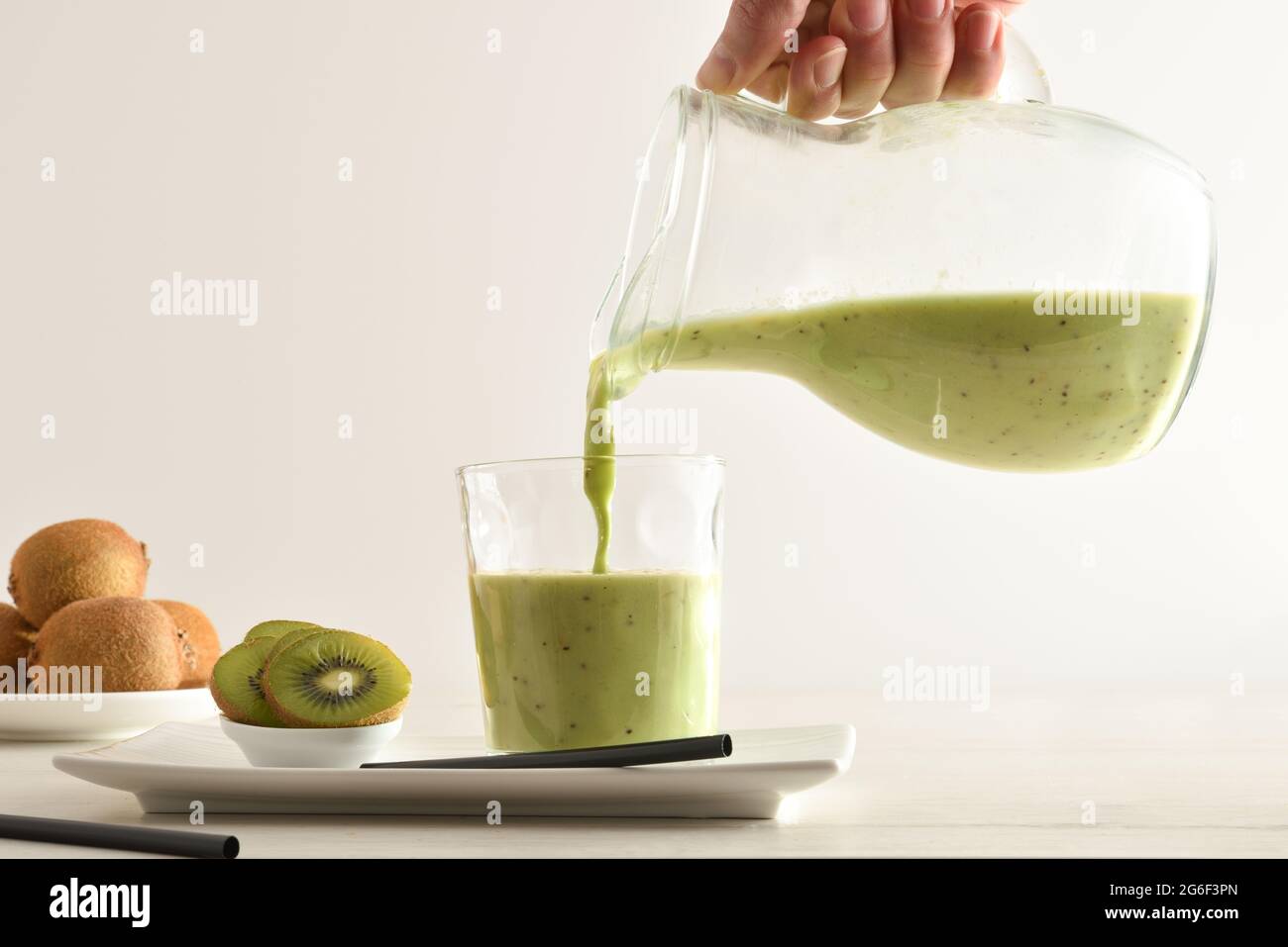 Person, die Kiwi trinkt aus Krug mit geschnittenem Obst in Behältern auf Küchenbank isoliert weiß. Vorderansicht. Stockfoto