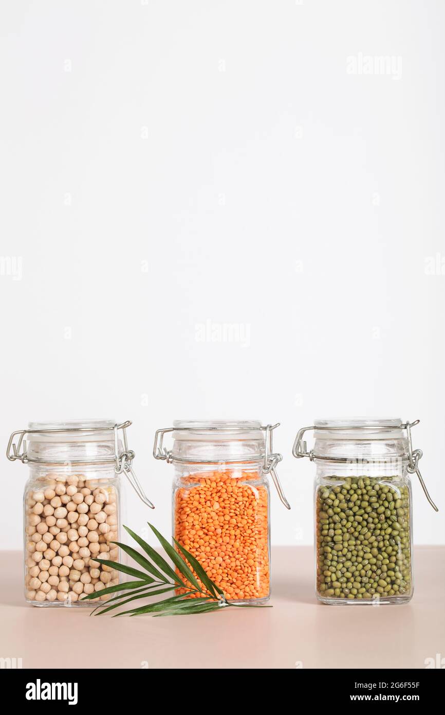 Vegane Proteinquelle. Kichererbsen, Linsen, Mungn in Gläsern auf weißem und beigem Hintergrund. Gesundes vegetarisches Essen. Platz kopieren Stockfoto