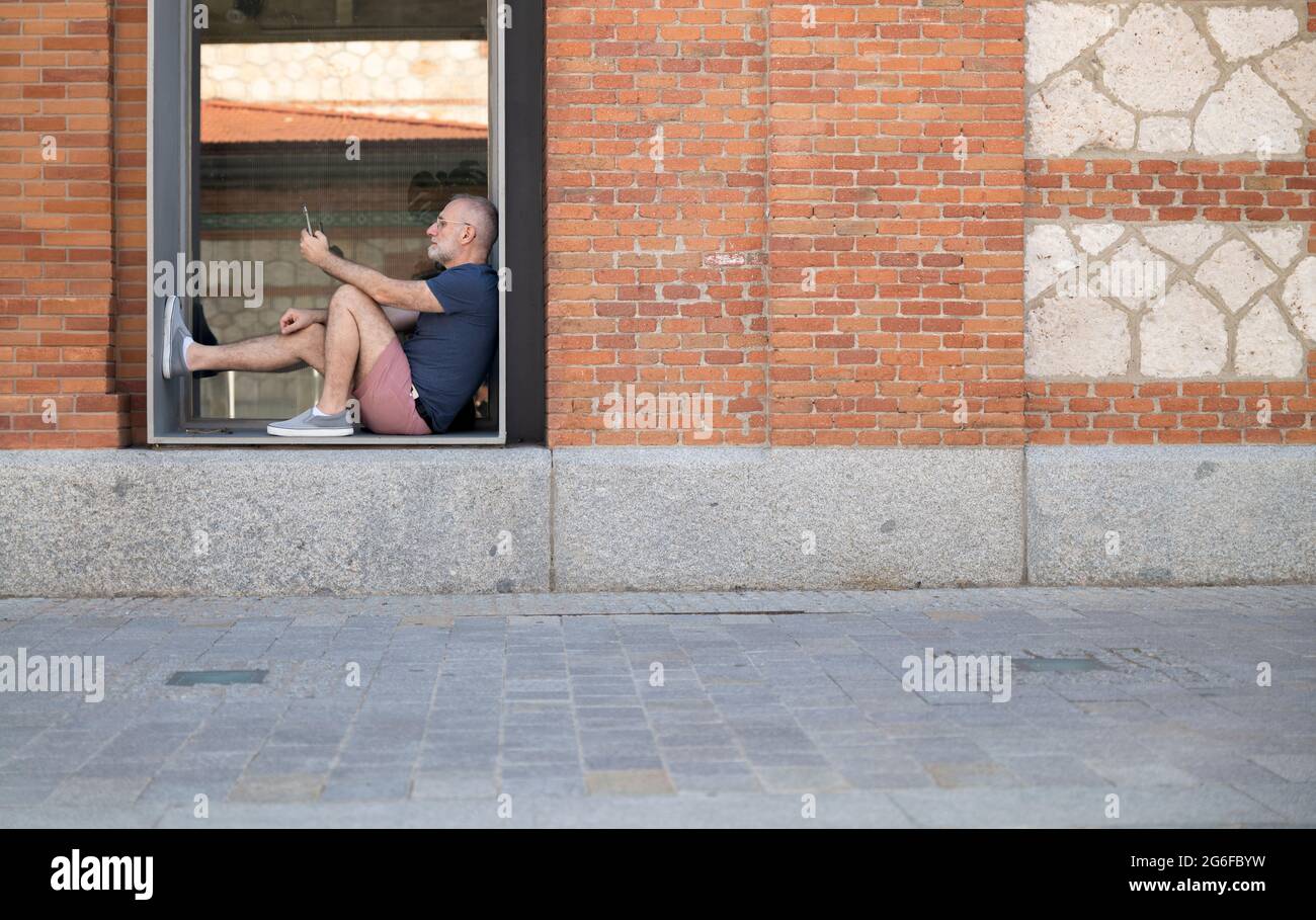 Mann, der das Handy im Fenster eines öffentlichen Gebäudes ansieht Stockfoto