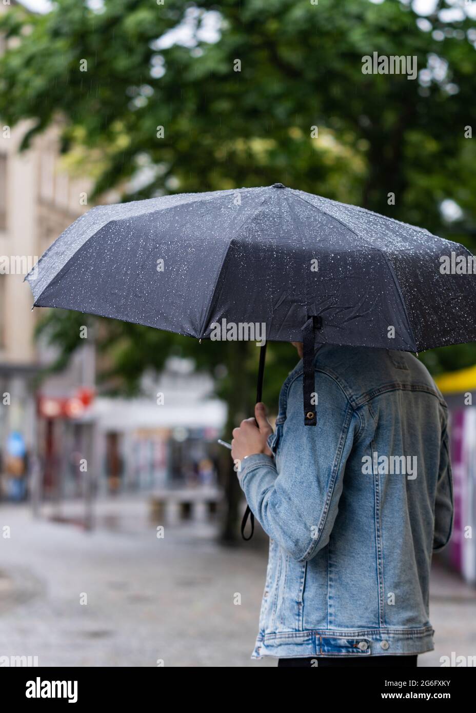 Schutz vor dem starken Sturmregen unter einem Regenschirm mit herunterlaufenden Wasserperlen. Telefoniert stand im Einkaufsviertel der Innenstadt. Stockfoto