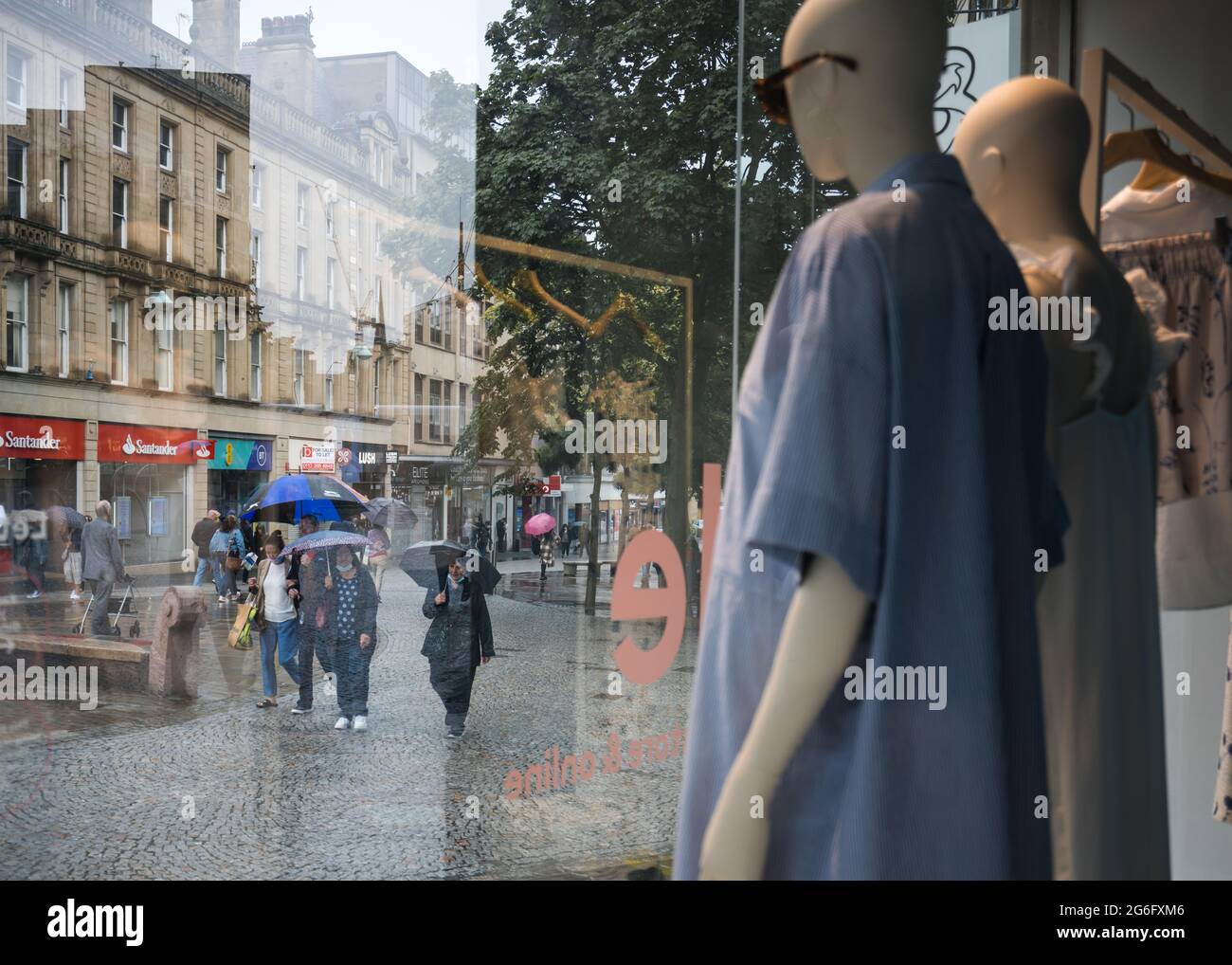 Schaufensterpuppe Dummies standen im Schaufenster in Sommerkleidung und Sonnenbrillen und beobachteten die Käufer auf der Hauptstraße, die an regenkalten Regenschirmen vorbeigingen Stockfoto