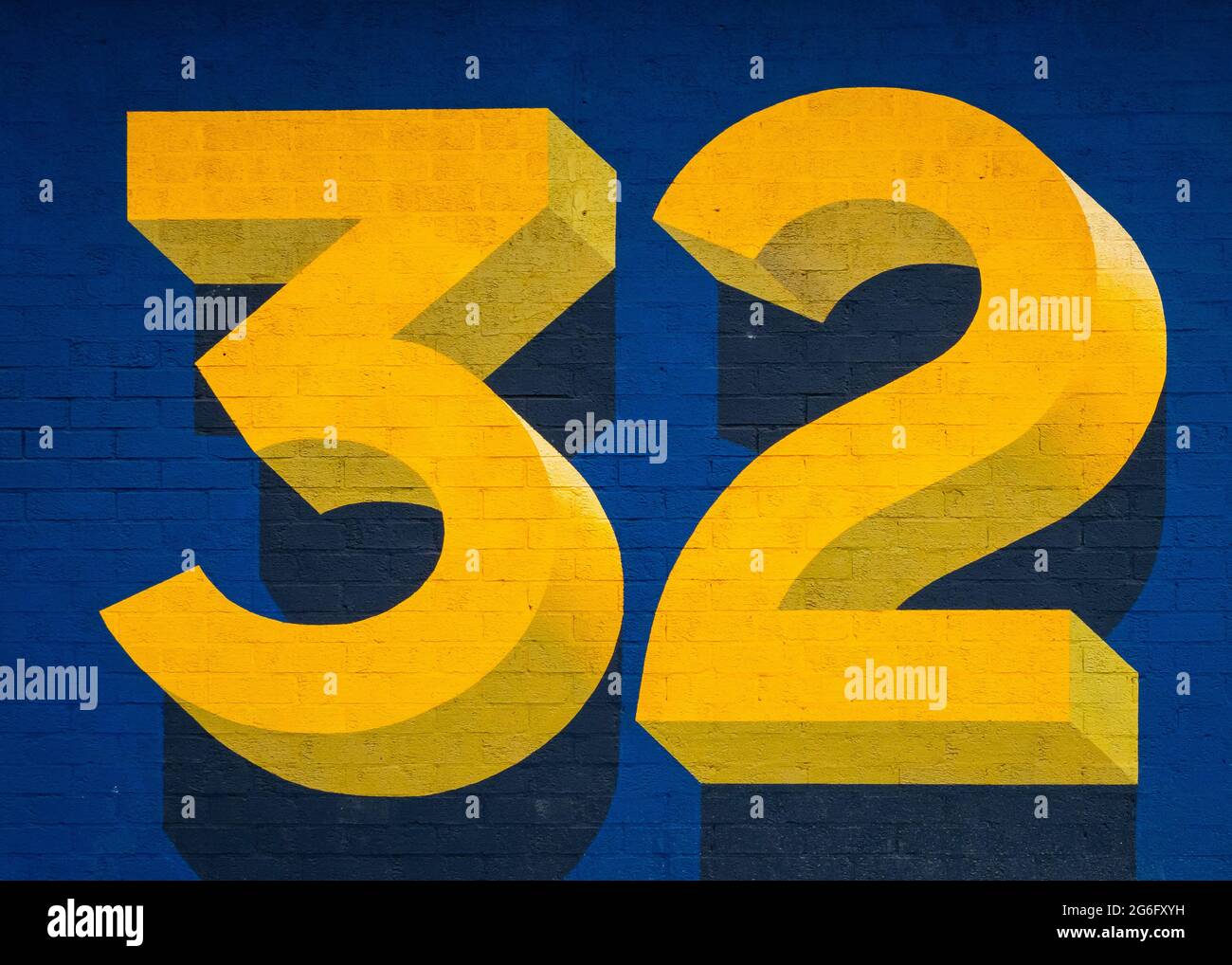 Große hellgelbe dreidimensionale Zahl zweiunddreißig auf blauem Hintergrund. 32 Ziffern in 3d drei und zwei. Ziegelstruktur. Stockfoto