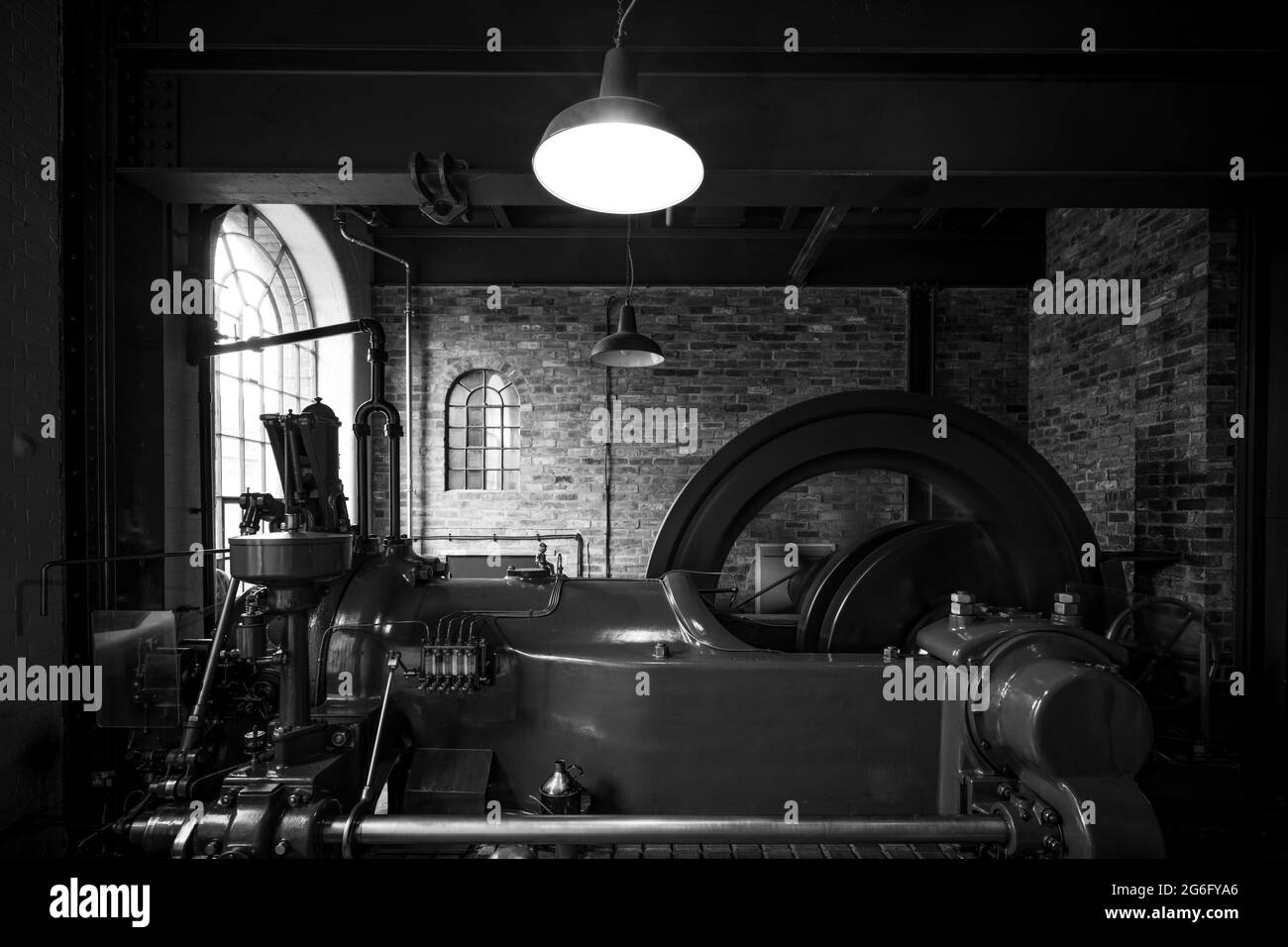 Alte Dampfmaschine läuft mit Rad in Bewegung. Industrielle Umgebung Mauerwerk und Werkseinstellung. Rad dreht sich mit hoher Geschwindigkeit. Stockfoto