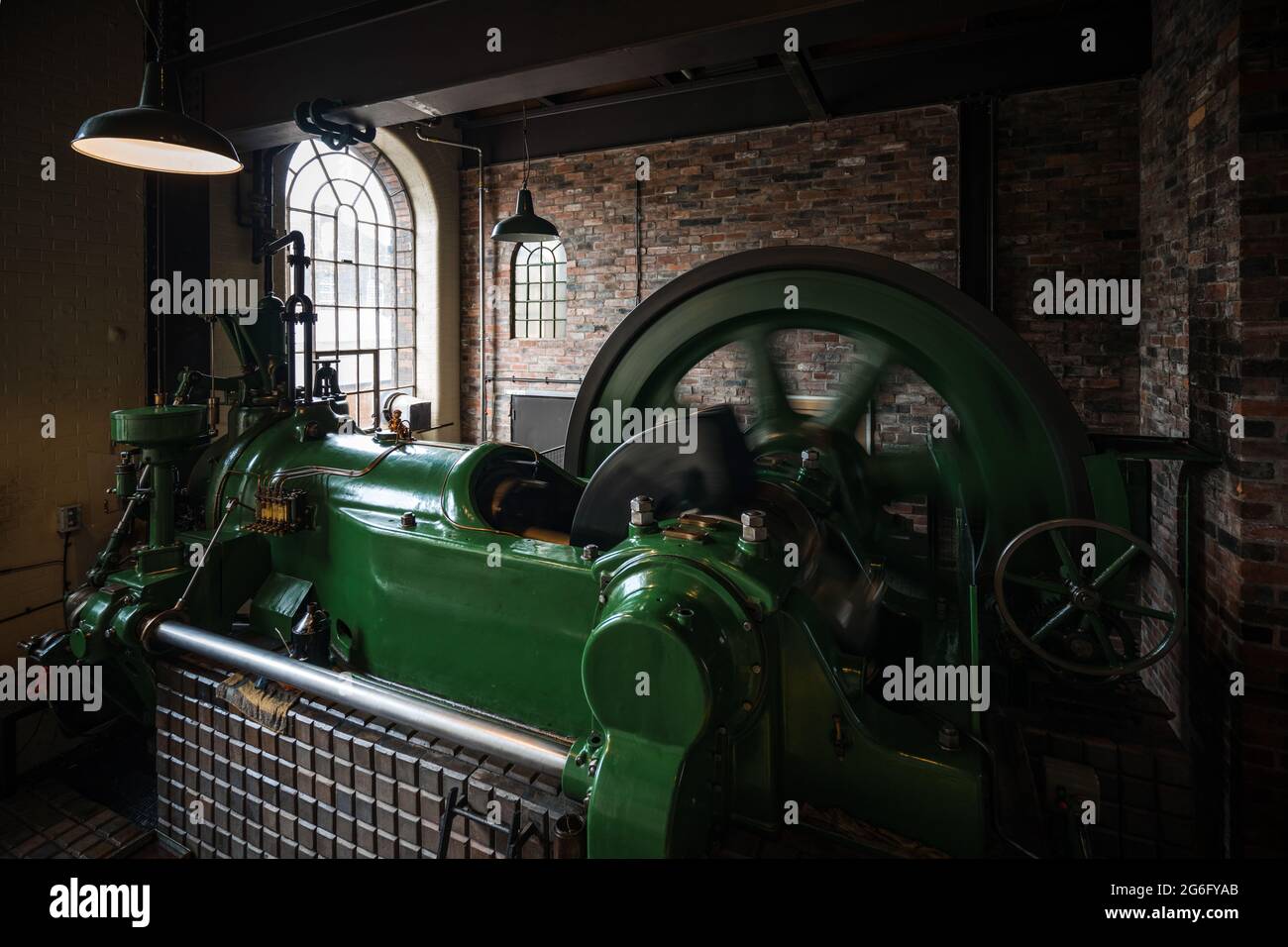Alte Dampfmaschine läuft mit Rad in Bewegung. Industrielle Umgebung Mauerwerk und Werkseinstellung. Rad dreht sich mit hoher Geschwindigkeit. Stockfoto