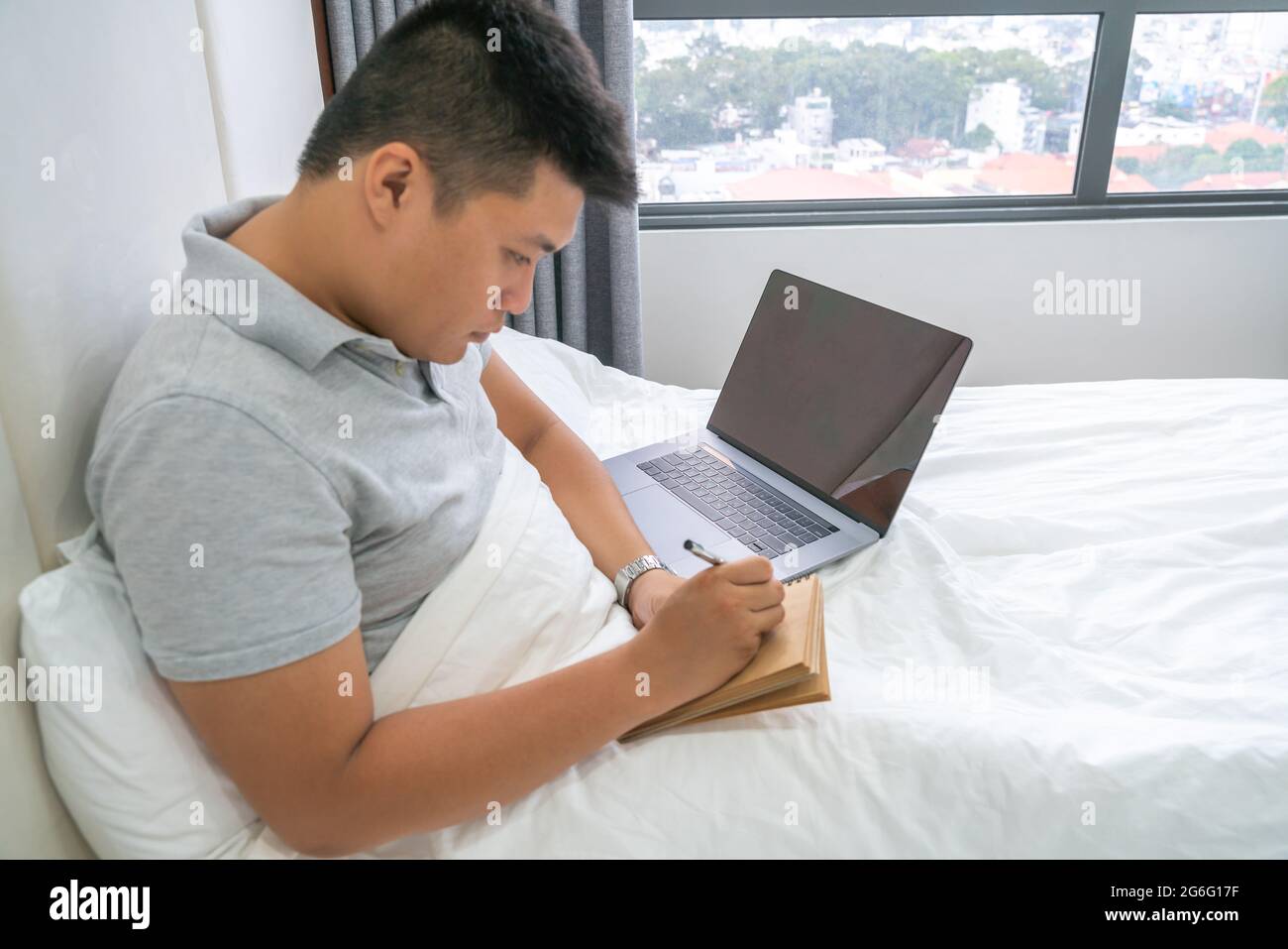 Seitenansicht eines jungen Mannes, der Notizen auf dem Bett schrieb Stockfoto