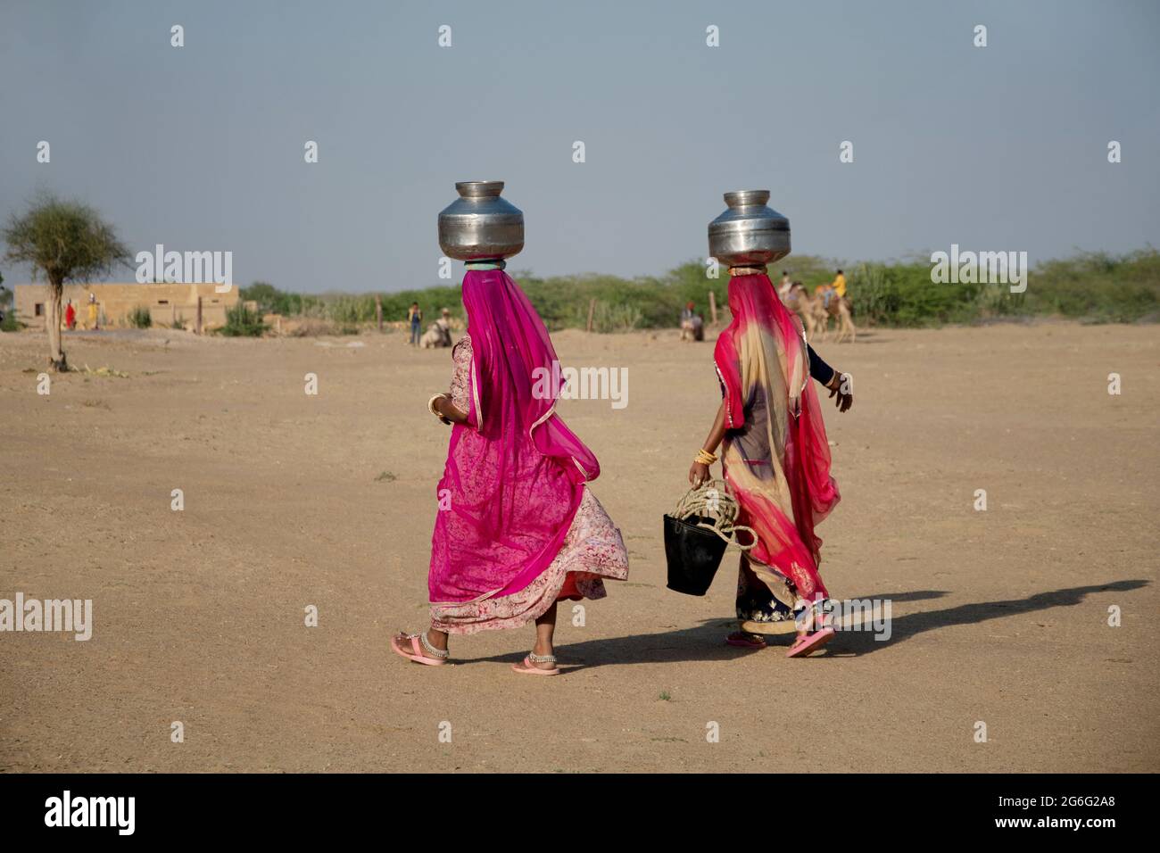 Zwei Frauen, die Wasser in Stahlbehältern auf dem Kopf in der Wüste, Khuri, Rajasthan, Indien, tragen Stockfoto