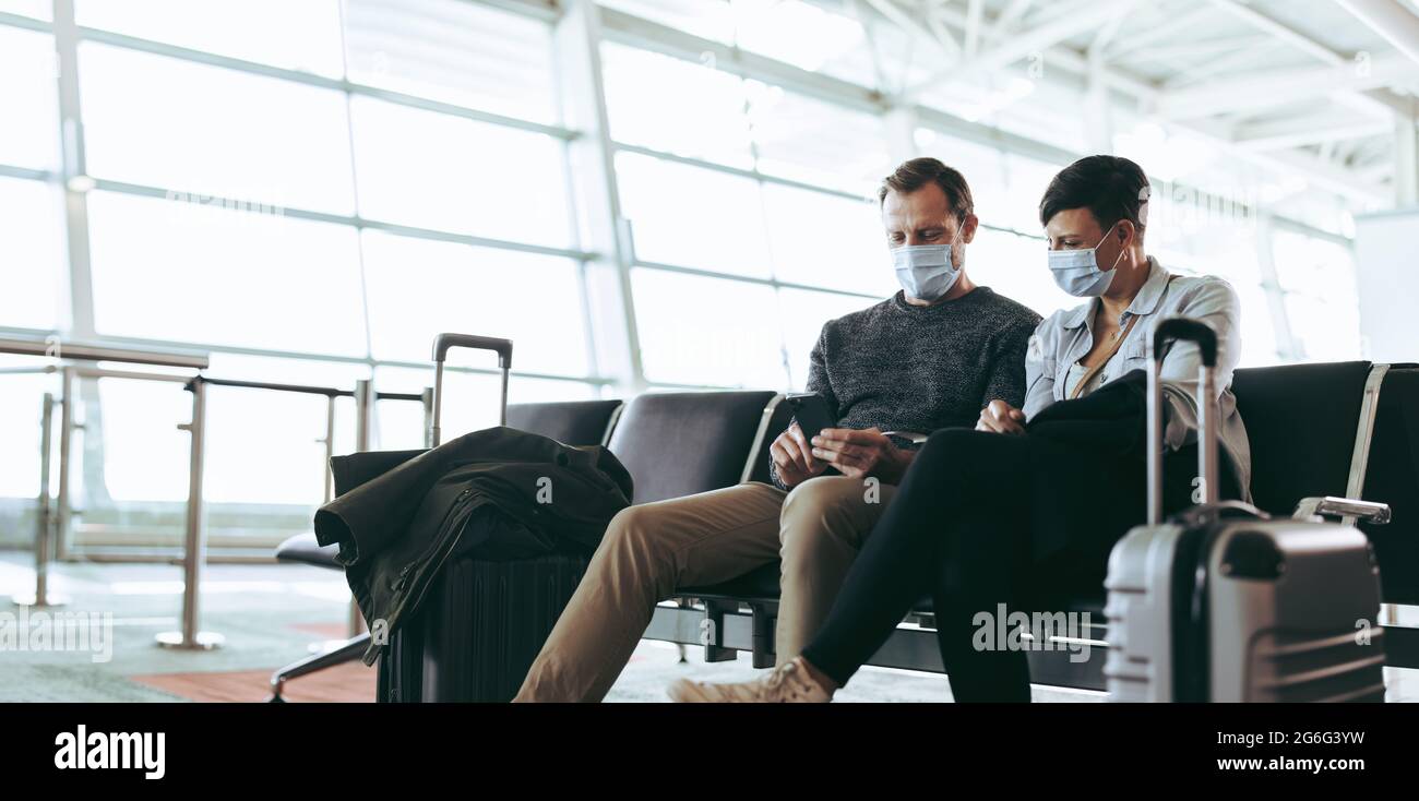 Touristen in Masken am Flughafen warten auf verspätete oder annullierte Flüge aufgrund von covid-19-Lockdown. Reisende prüfen Fluginformationen online mit Smar Stockfoto