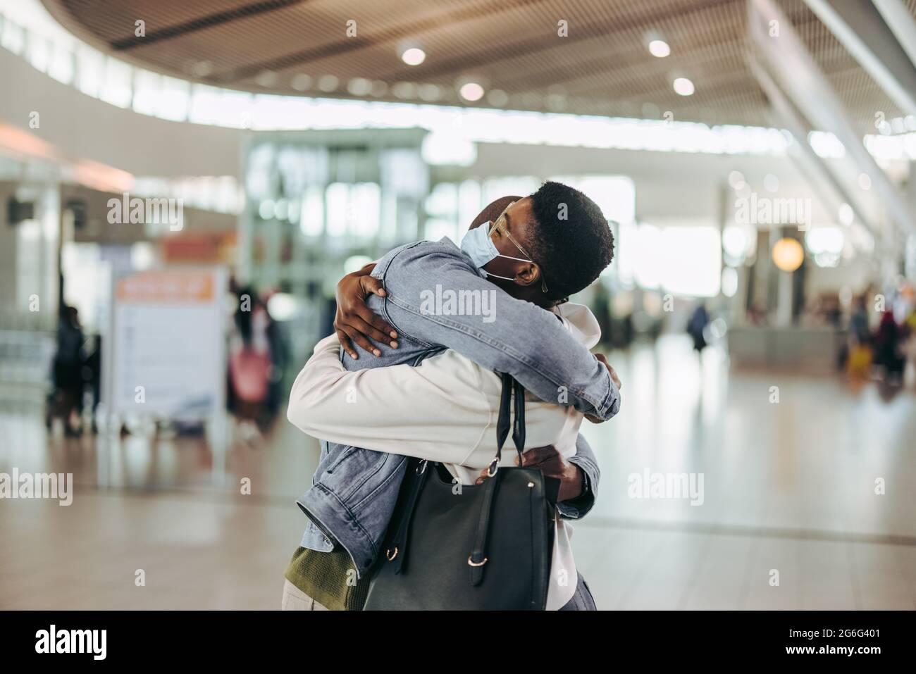 Reisender Mann und Frau, die sich am Ankunftstor des Flughafens herzlich umarmen. Frau, die am Flughafen eine warme Willkommensumarmung bekommt. Stockfoto