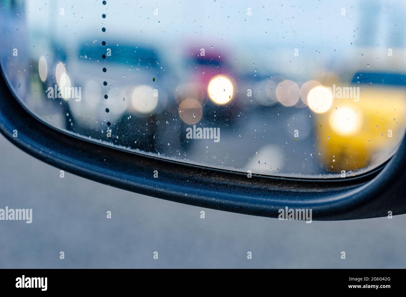 Viele verschwommene Lichter von Autos, die in der Schlange stehen, vom nassen und schmutzigen Rückspiegel mit Wassertropfen gesehen, Stau bei regnerischem Wetter - s Stockfoto