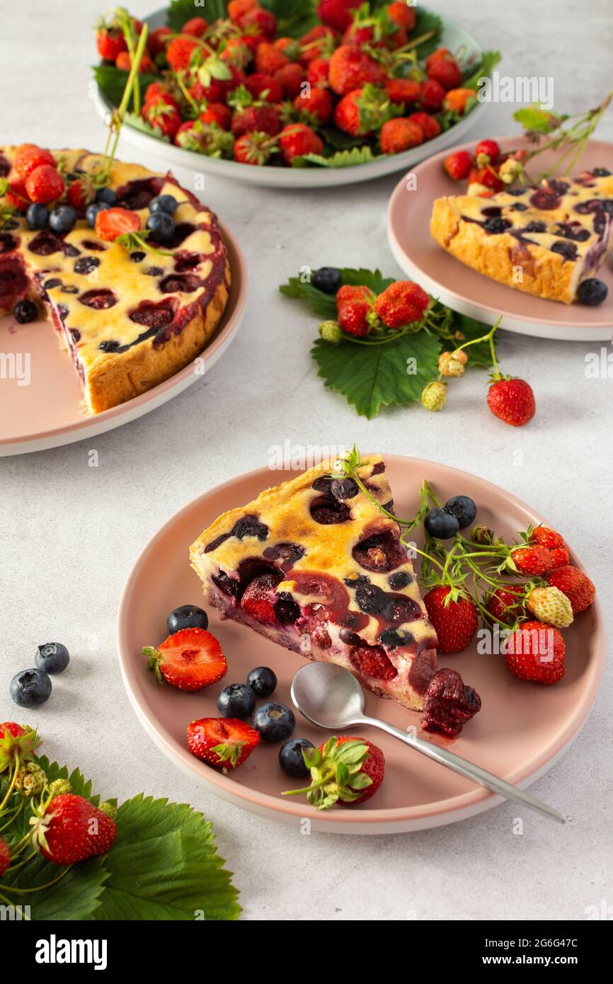 Stück Erdbeer-Blaubeerkuchen mit frischen Beeren auf einem rosa Teller auf grauem Hintergrund Stockfoto