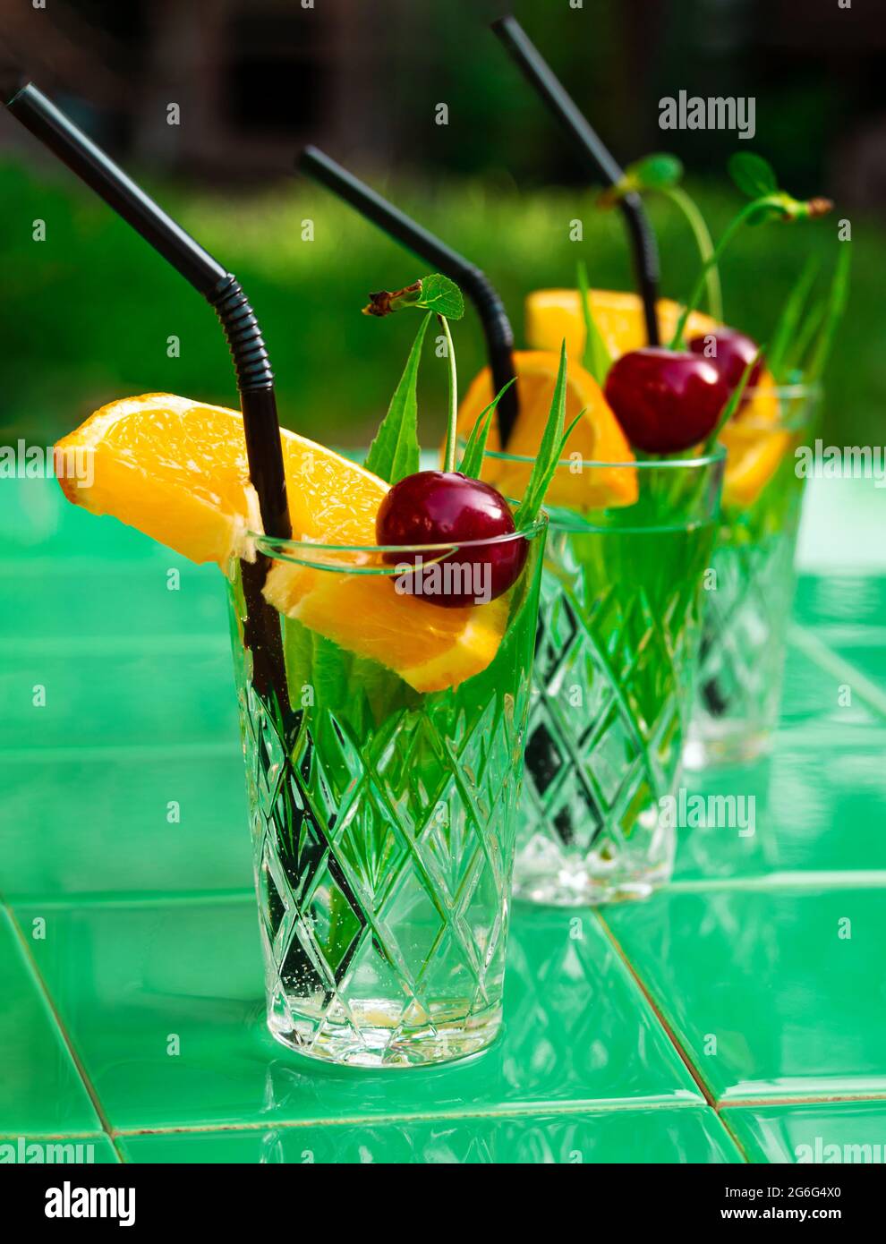 Erfrischende Getränke in Kristallgläsern grün Blätter kirschorange Scheibe Fliesen Hintergrund Schatten. Süßer, kalter natürlicher Cocktail an heißen Sommertagen. Sodawasser Stockfoto