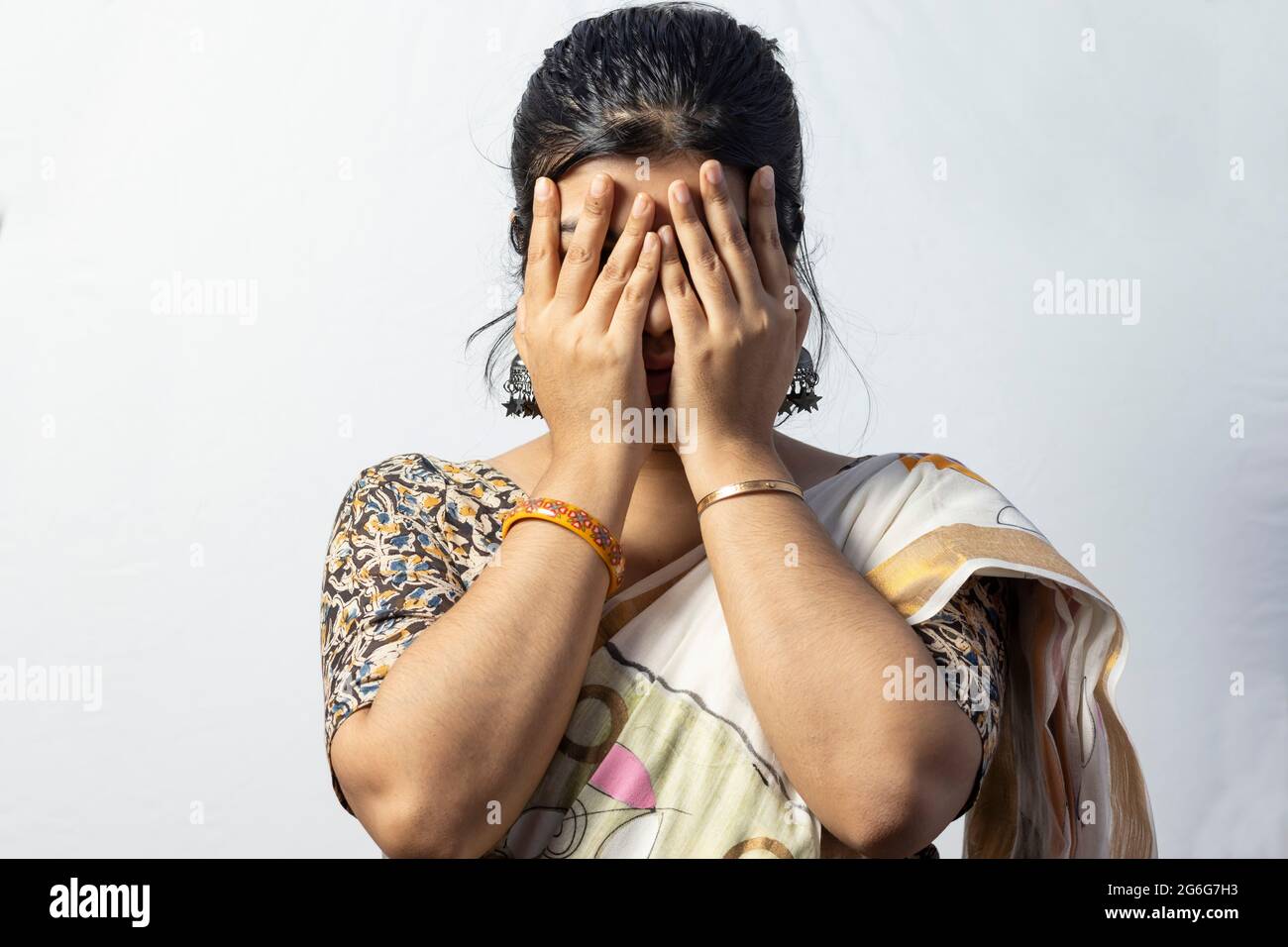 Isoliert auf weißem Hintergrund ein indisches weibliches Gesicht bedeckt mit Händen auf weißem Hintergrund Stockfoto