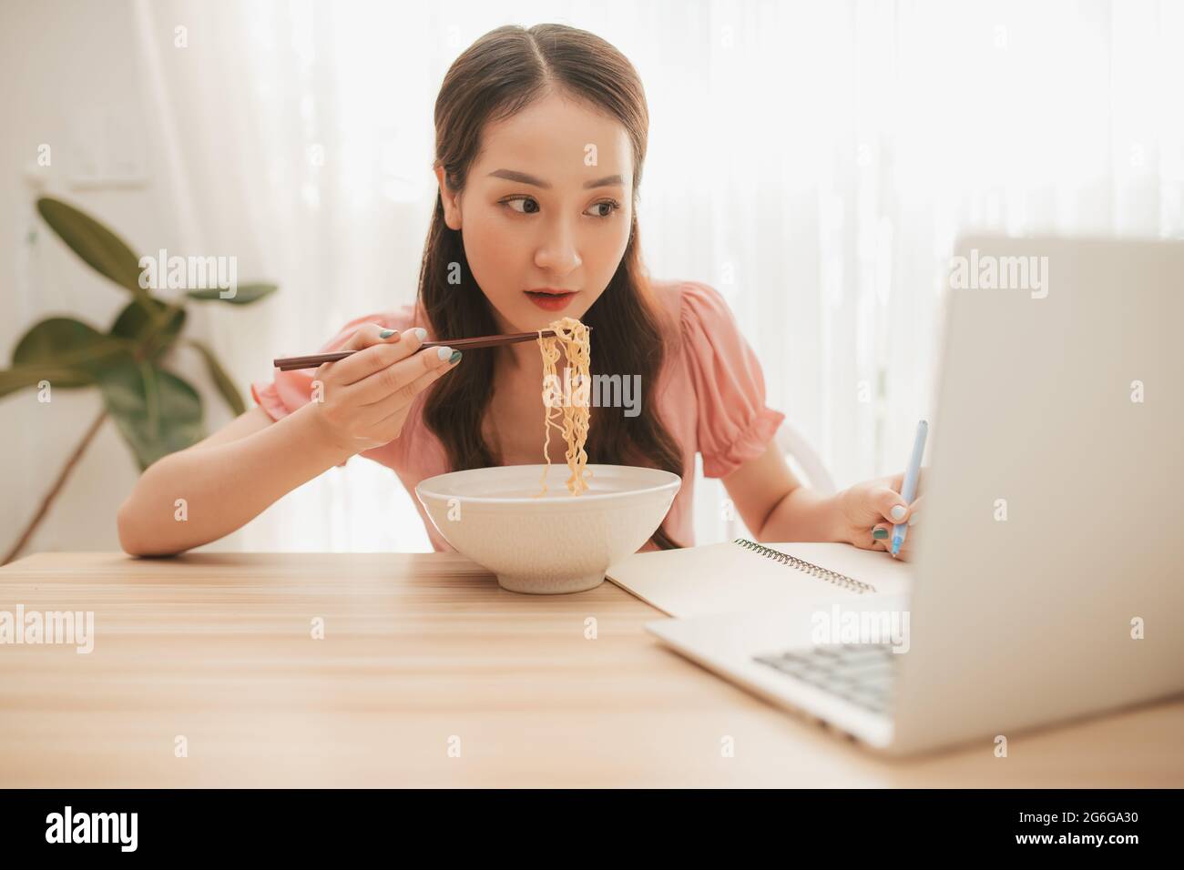 Weibliche Angestellte hält Essstäbchen essen Instant Nudel am Arbeitsplatz in Heimbüro Stockfoto