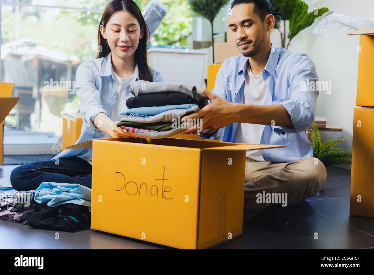 Spendenkonzept. Liebespaar Frau und Mann legen Kleidung, um Box mit voller Kleidung zu spenden Stockfoto