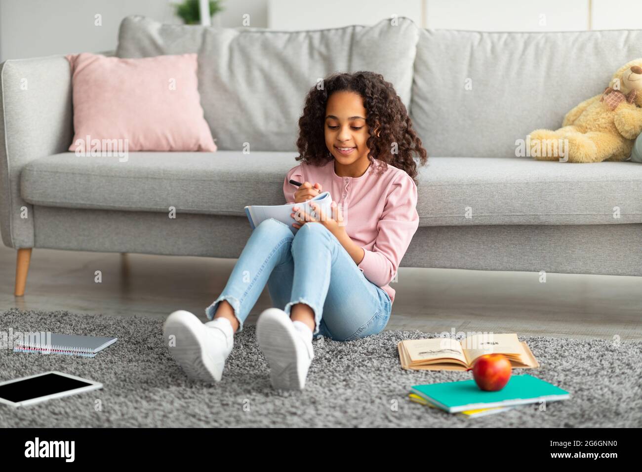 Positive afroamerikanische Teenager Mädchen Hausaufgaben machen, Notizen machen oder Essay schreiben, sitzen im Wohnzimmer Innenraum Stockfoto