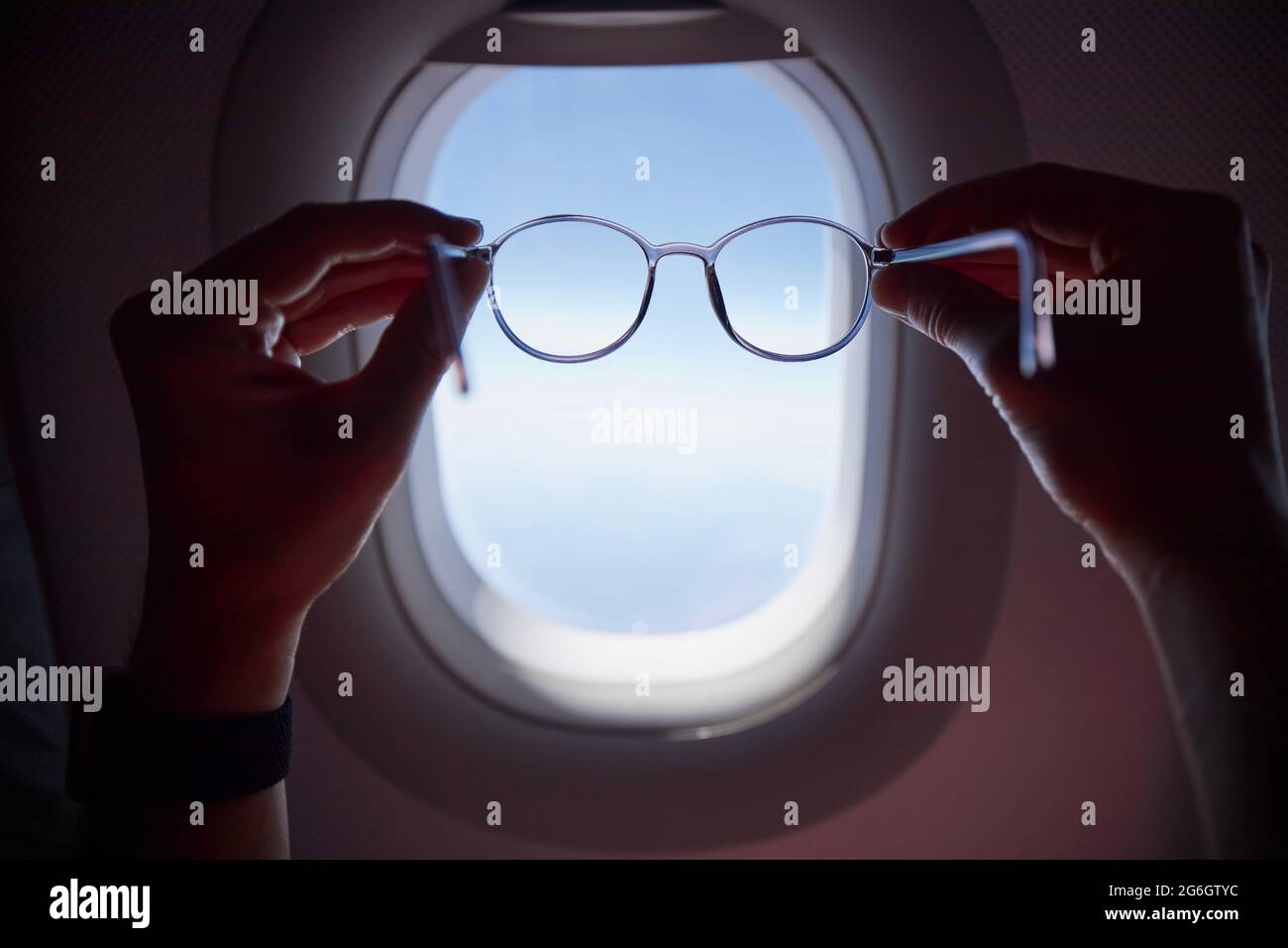 Hand des Passagiers, der während des Fluges eine Brille gegen das Flugzeugfenster hält. Themen Reisen, Sehvermögen und Vision. Stockfoto