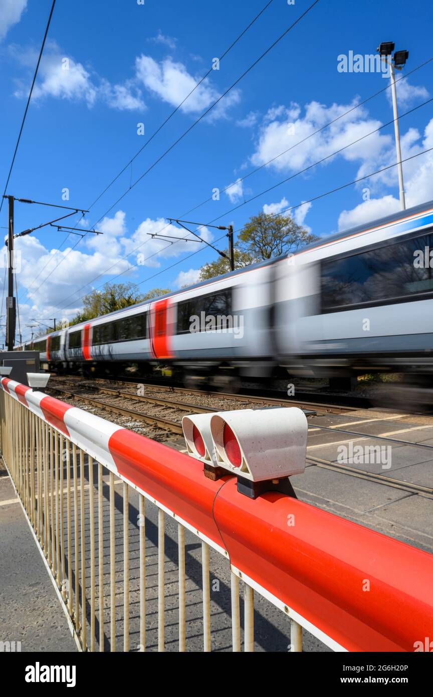 Zug, der in Essex, England, durch einen Bahnübergang mit Geschwindigkeit fährt. Stockfoto