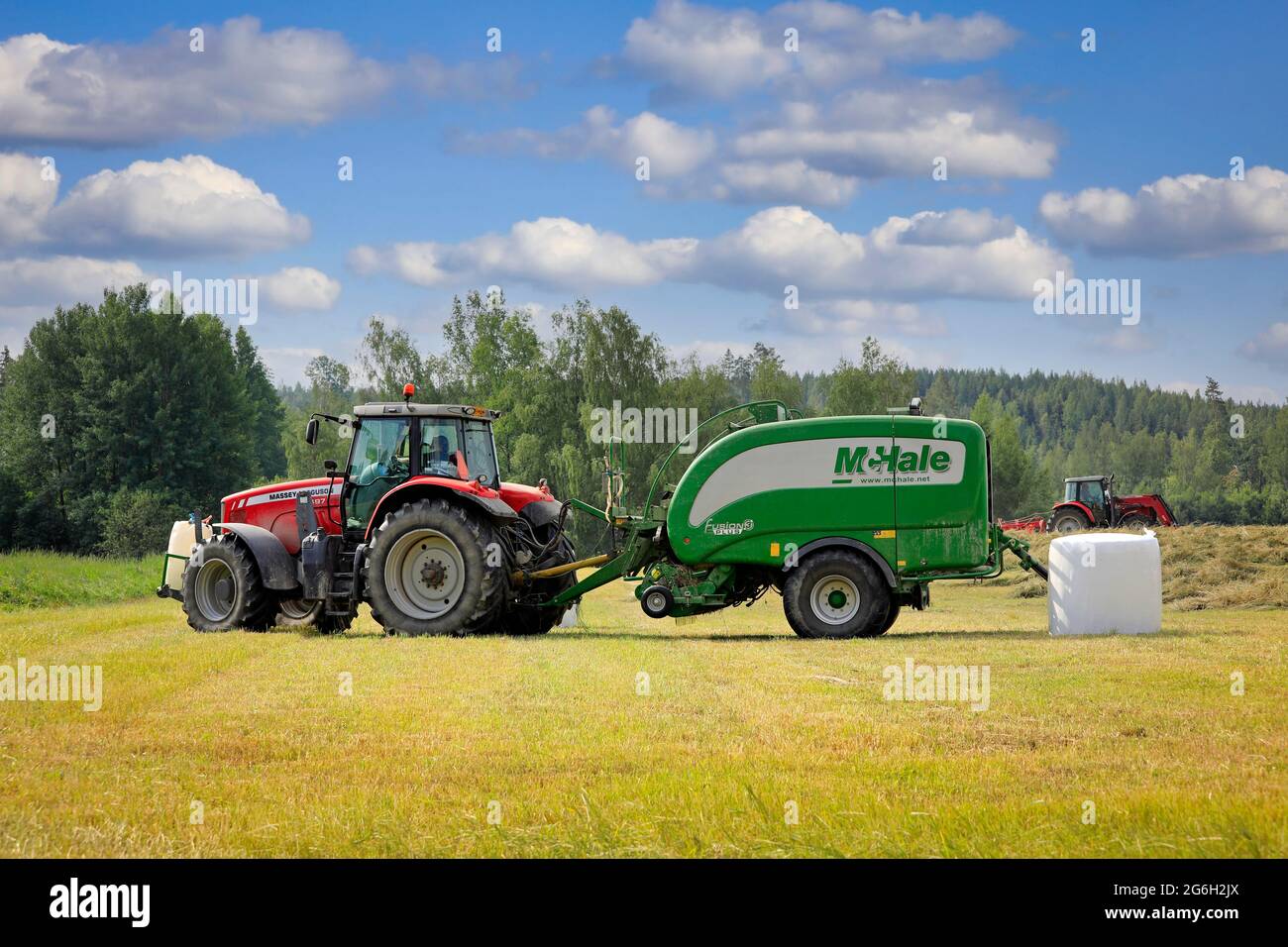 Massey-Ferguson-Traktor im Heufeld mit McHale-Ballenwickler, der im Sommer trockenes Heu erntet. Raasepori, Finnland. 25. Juni 2021. Stockfoto