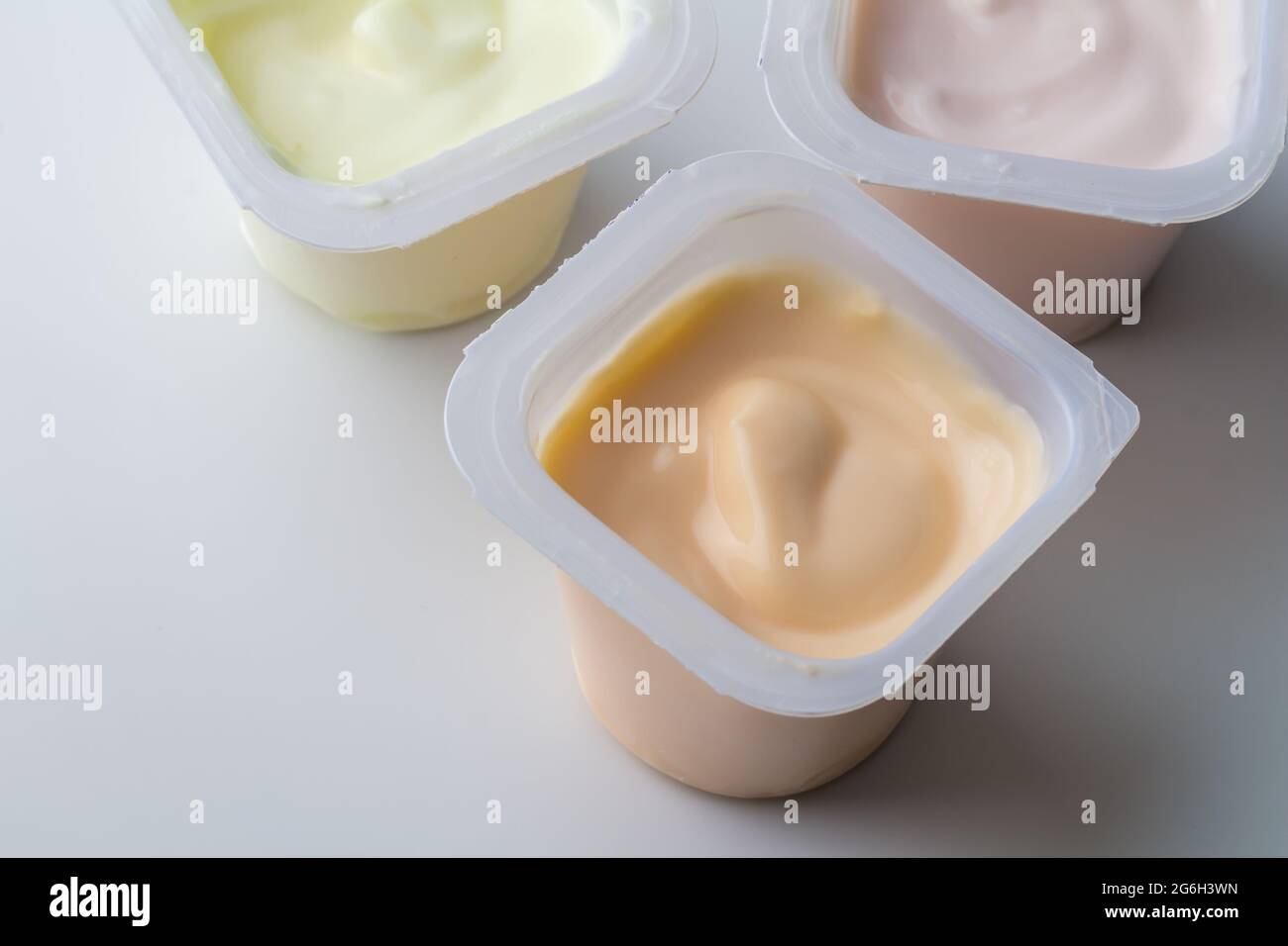 Aromatisierter Joghurt in Kunststofftöpfen - bunte Joghurtbecher mit Fruchtgeschmack auf Weiß isoliert mit Kopierfläche - Foto von oben Stockfoto