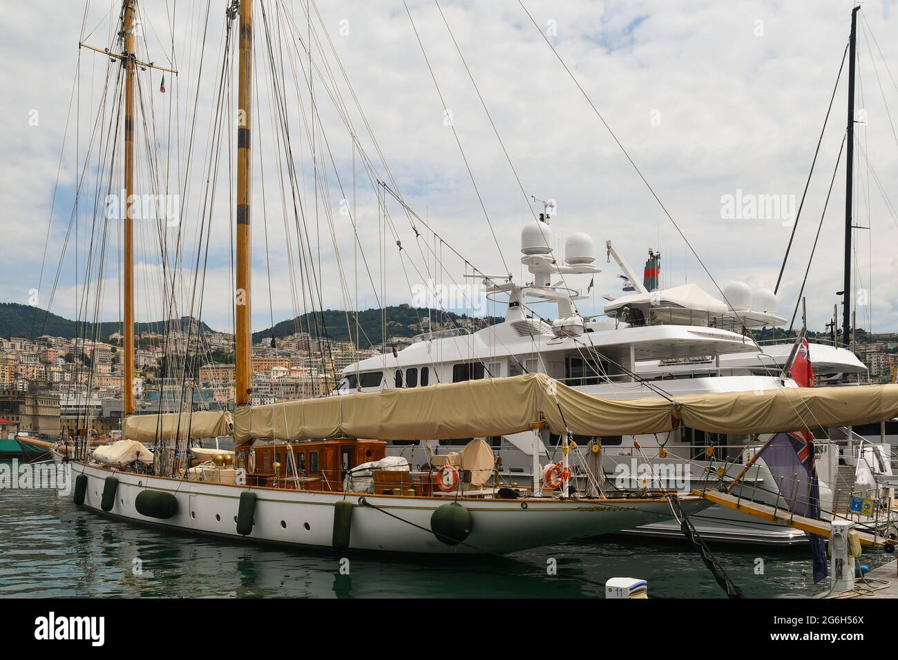 Ein Segelboot im Vintage-Stil und eine moderne Yacht, die im Alten Hafen (Porto Antico) von Genua mit der Stadt im Hintergrund, Ligurien, Italien, festgemacht ist Stockfoto