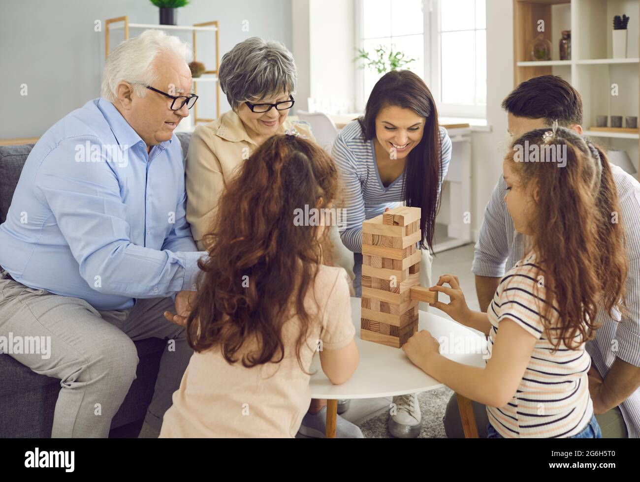 Die glückliche große Familie spielt zu Hause Jenga und wechselt sich ab, indem sie Ziegelsteine aus einem Holzturm herausholt. Stockfoto