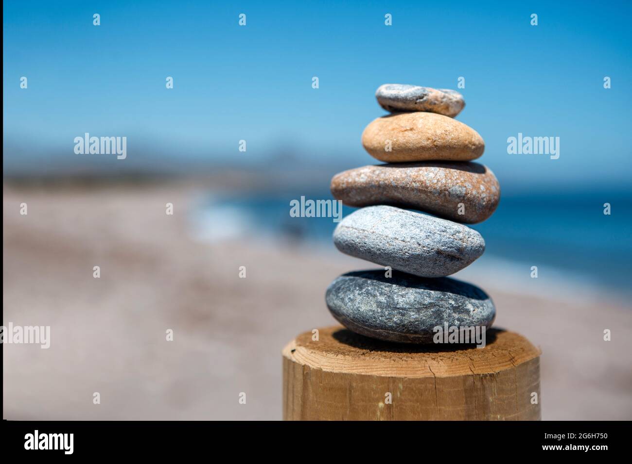Gleichgewicht und Schönheit in einer pyramidenförmigen Form von fünf Steinen, die übereinander in Balance gebracht werden, mit Blick auf das Meer, was Frieden und visuelle Harmonie gibt. Stockfoto