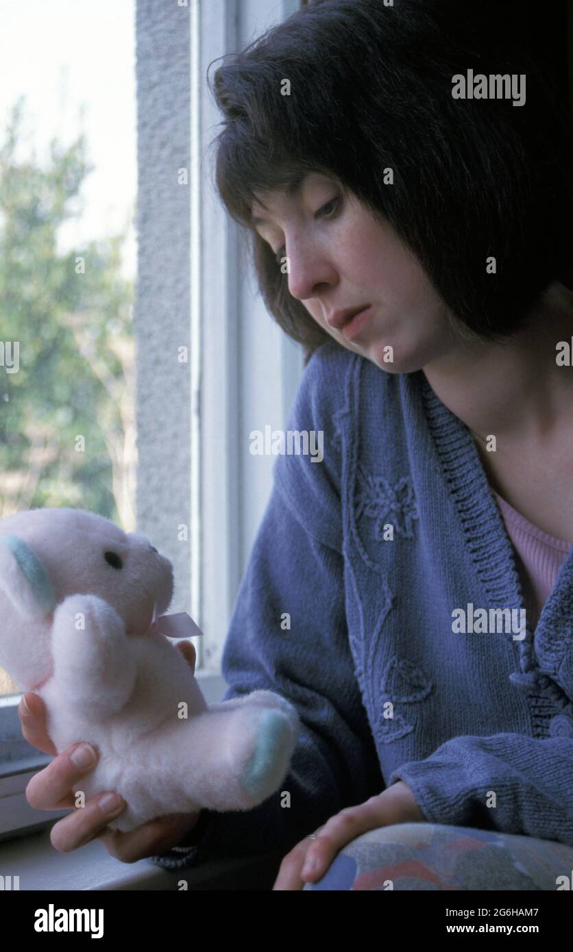 Unglückliche Frau, die am Fenster sitzt und Teddybär hält Stockfoto