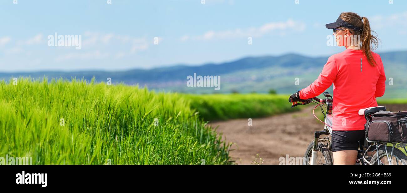 Eine Frau, die im Sommer auf dem grünen Feld Fahrrad fährt Stockfoto