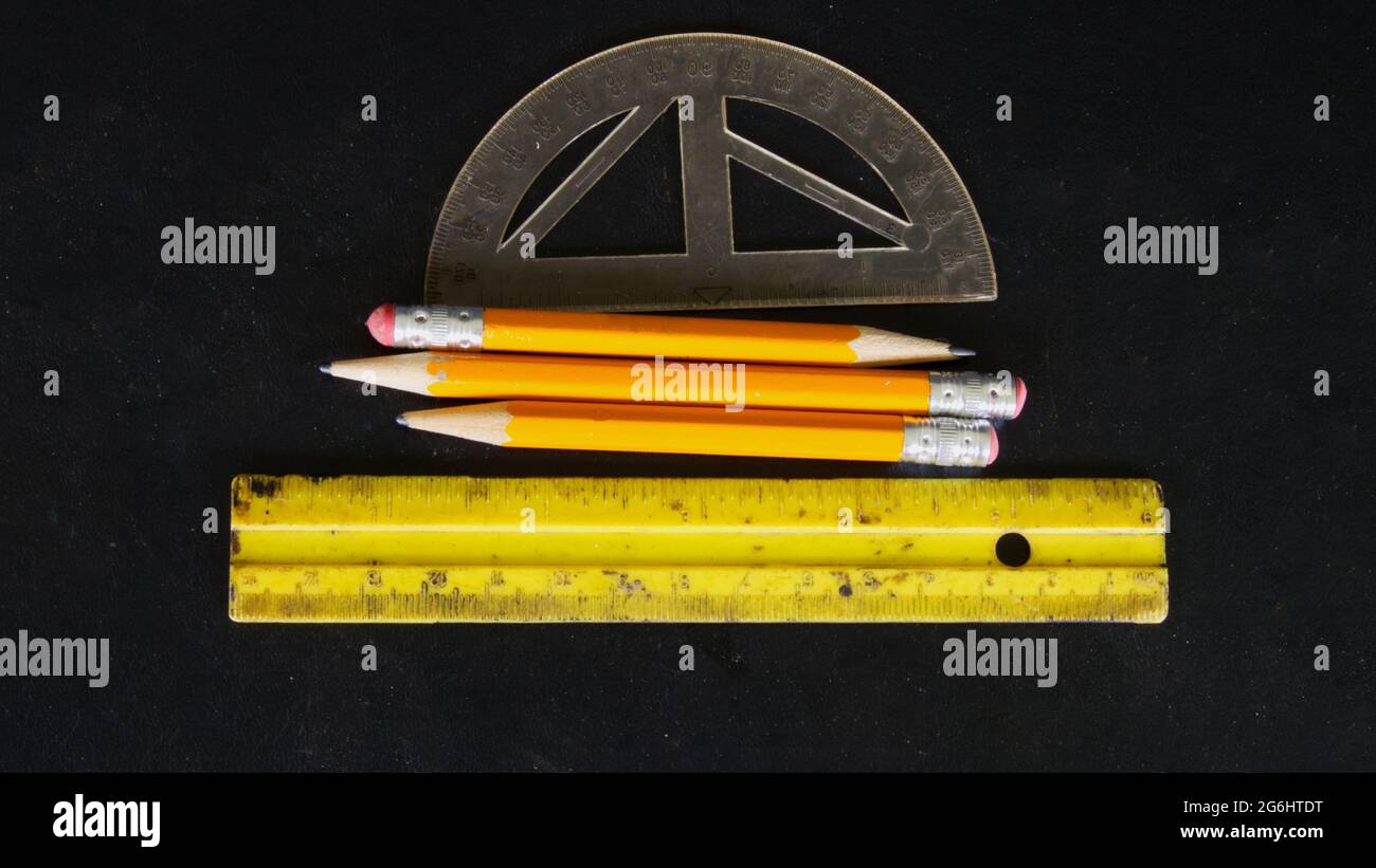 Drei Bleistifte, Winkelmesser und ein Lineal auf einem schwarzen Backgrouns Stockfoto