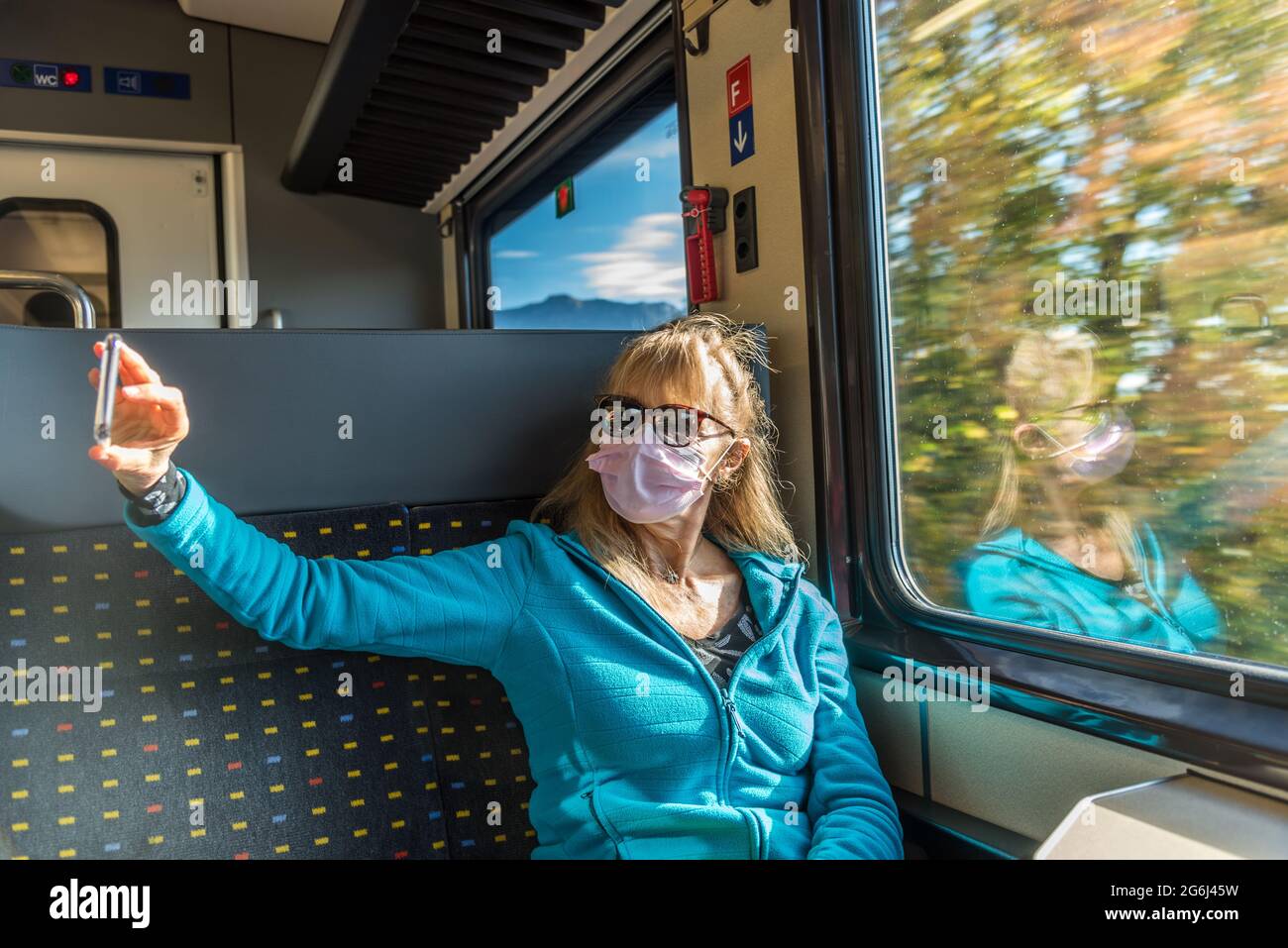 Glückliche Frau mit Gesichtsmaske, die mit dem Zug unterwegs ist und ein Selfie mit ihrem Telefon macht. Stockfoto