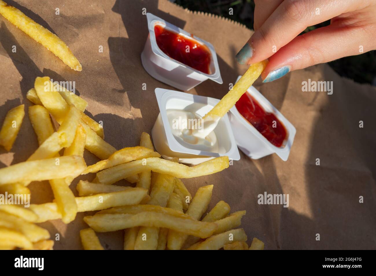 Pommes frites in Ketchup und Mayonnaise eintauchen. Essen zum Mitnehmen und Picknick-Konzept.Essen in Quarantäne.schädliche Lebensmittel und ungesunde Diäten. Stockfoto