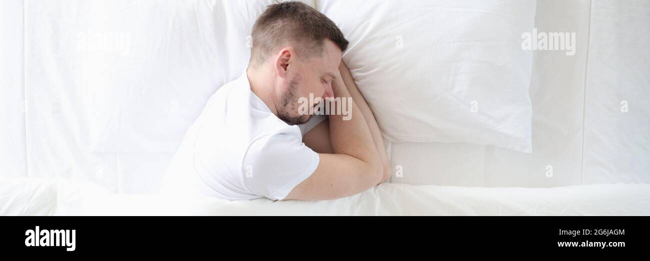 Der junge Mann schläft friedlich auf dem großen weißen Bett Stockfoto
