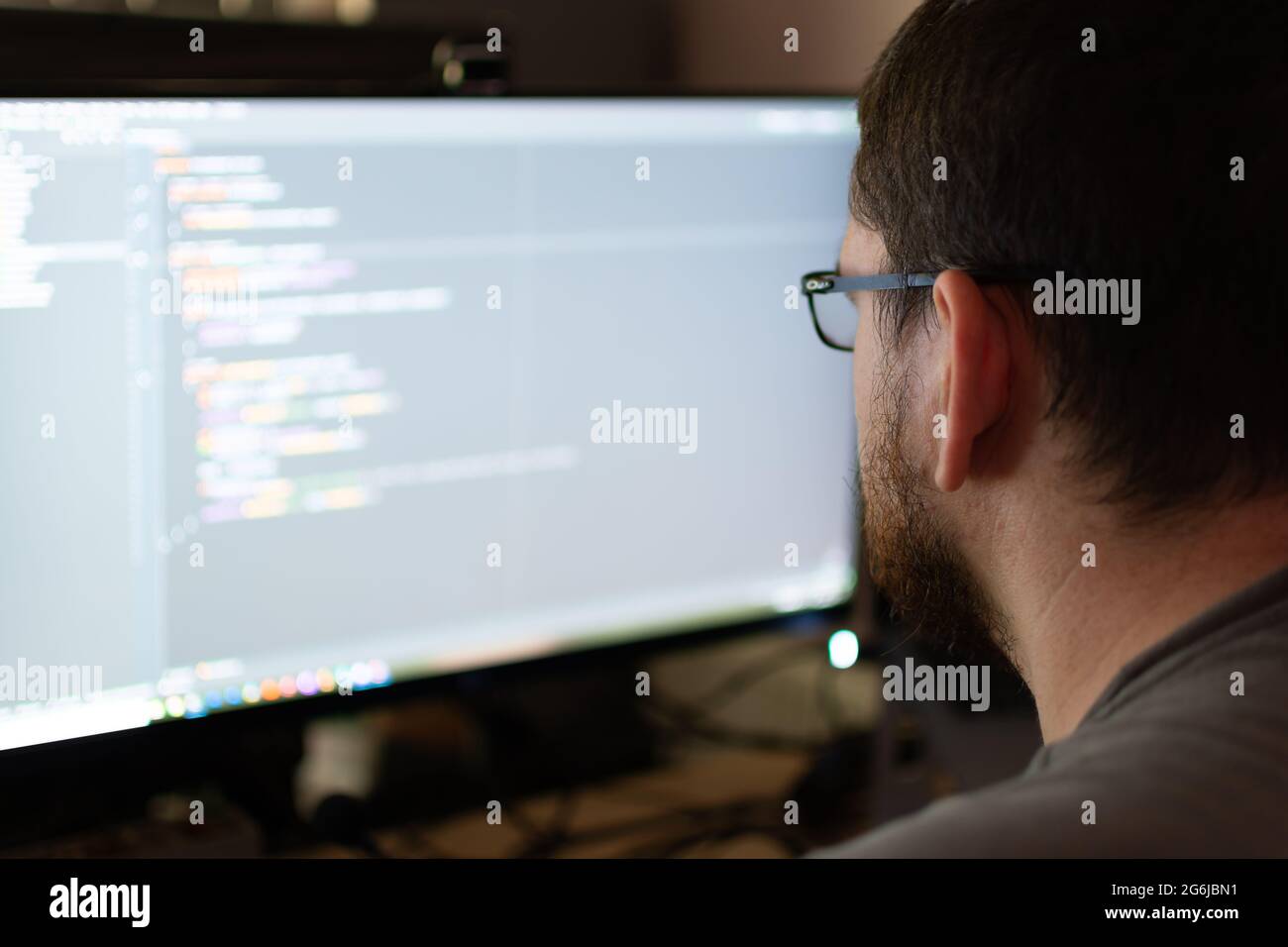 Eine über die Schulter-Ansicht eines Software-Ingenieurs in einer häuslichen Umgebung Debugging-Code. Der Ingenieur hat einen Bart und eine Brille. Stockfoto