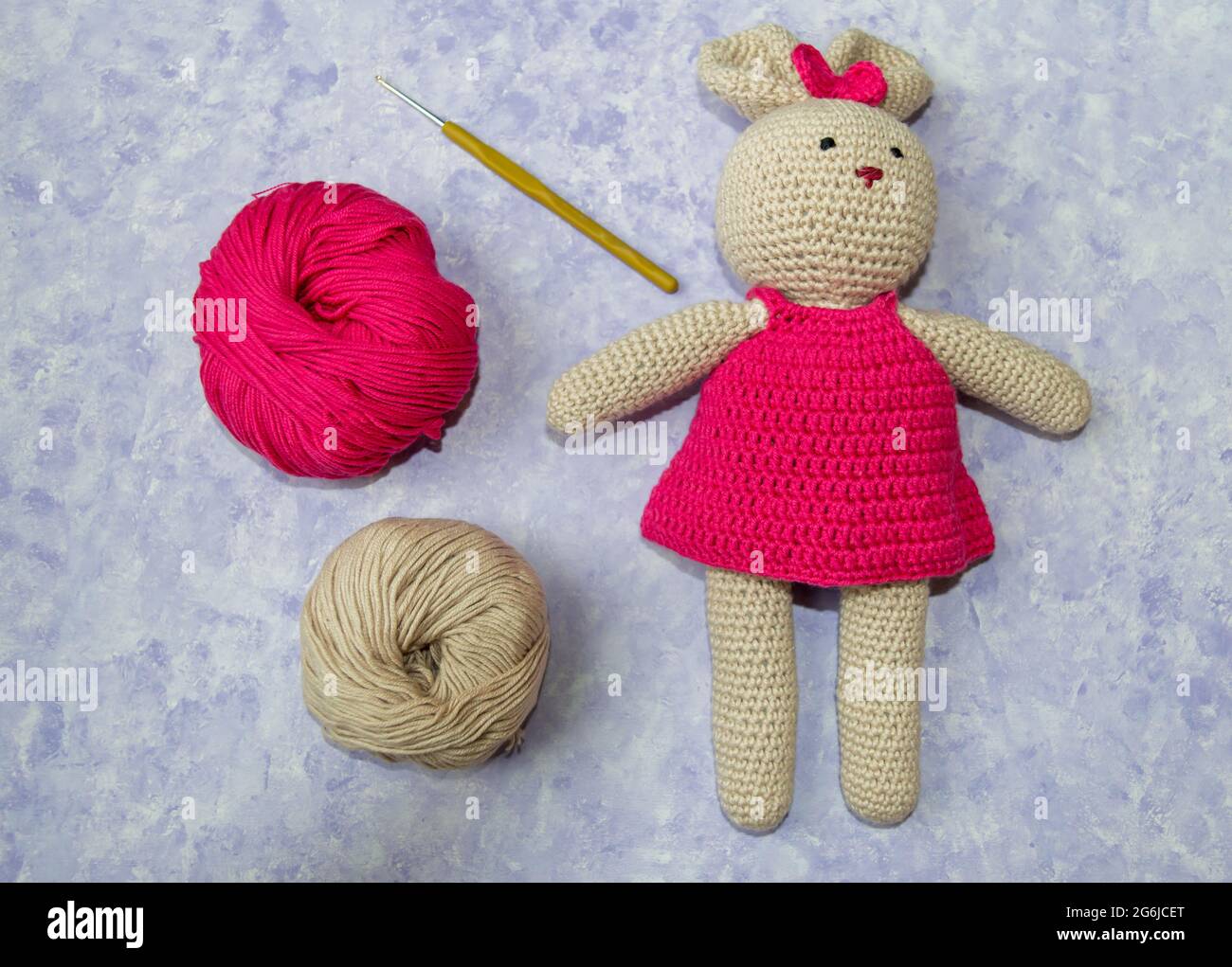 Rosa und beige Strickwolle, Kaninchen-Amigurumi und Häkelhaken auf blauem pastellfarbenem Hintergrund.Amigurumi Stufen.Draufsicht.Handgestrickte Spielzeug. Amigurumi. Stockfoto