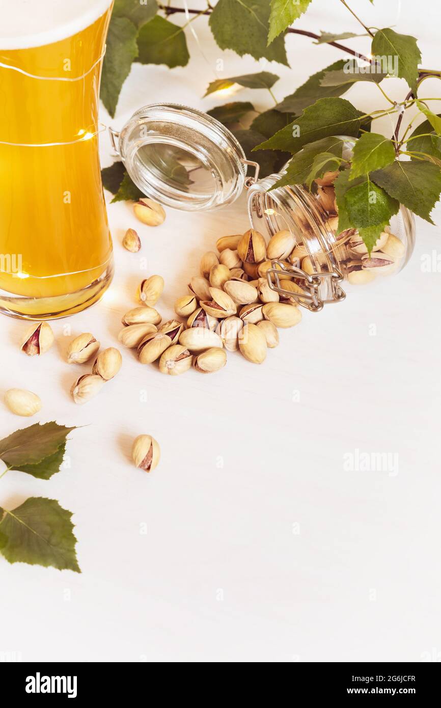 Vertikales Banner mit einem Glas kalten, natürlichen, leichten, ungefilterten Bieres, Gläsern mit Pistazien und Blättern auf weißem Hintergrund. Sommerfest Stockfoto