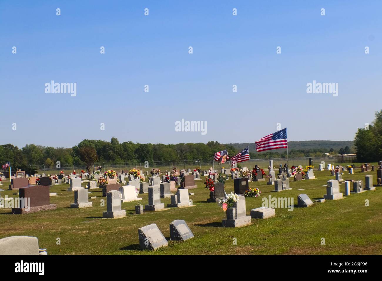 Amerikanische Flaggen, die über dem Friedhof fliegen, geschmückt mit Blumen für den Memorial Day in den Vereinigten Staaten mit Hügeln im Hintergrund Stockfoto