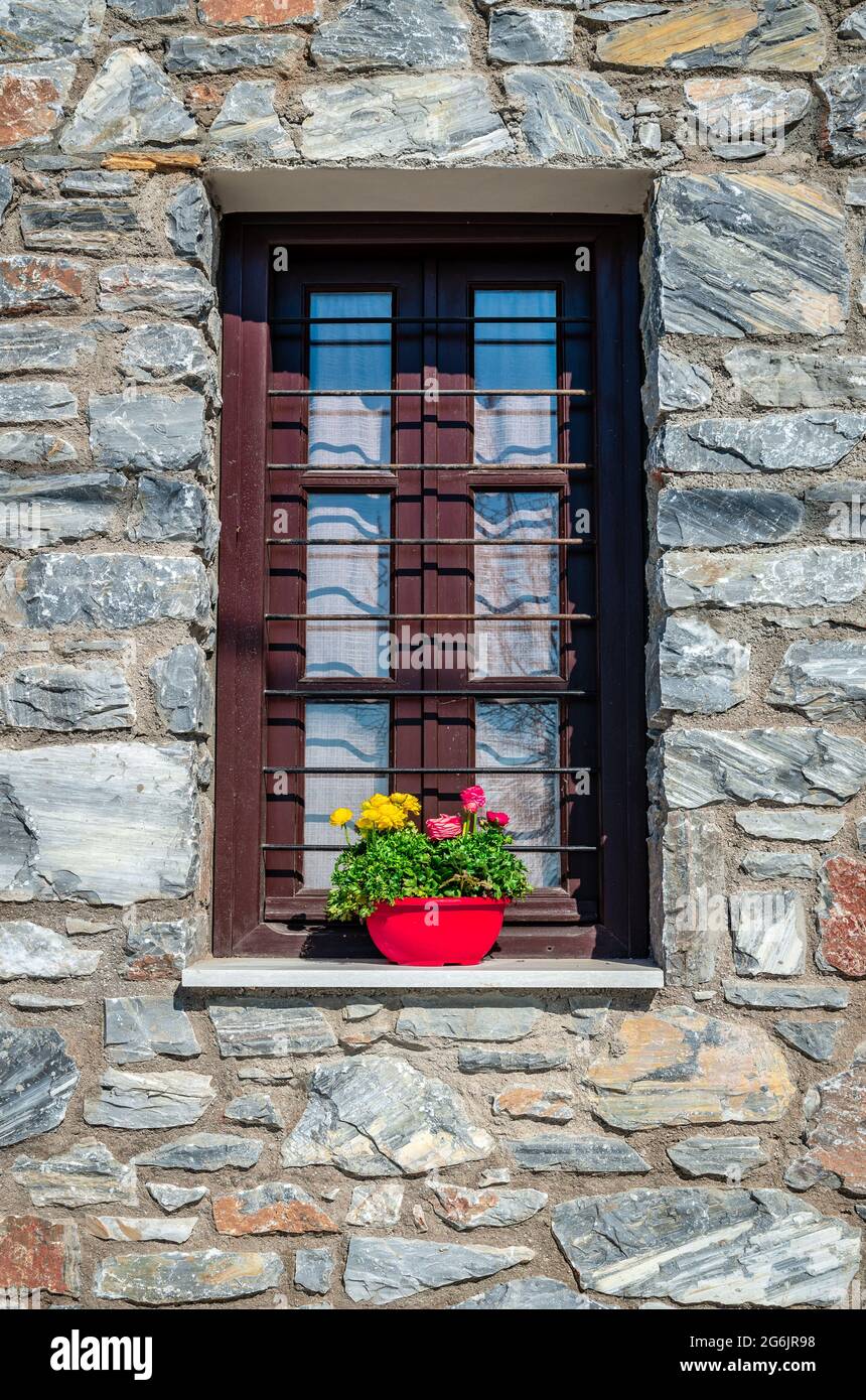 Fenster mit hölzernen Fensterläden verziert mit blühenden Blumen in einem Topf. Traditionelles Steinhaus in Afissos, an den Hängen des Berges Pelion, in Gr Stockfoto