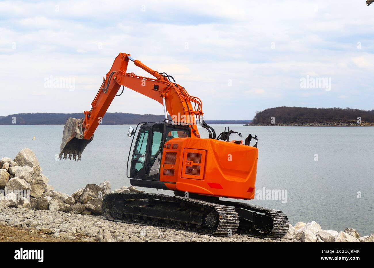 Glänzend neue orange Bagger auf Spuren am See Anordnung große Felsbrocken am Wasser Stockfoto