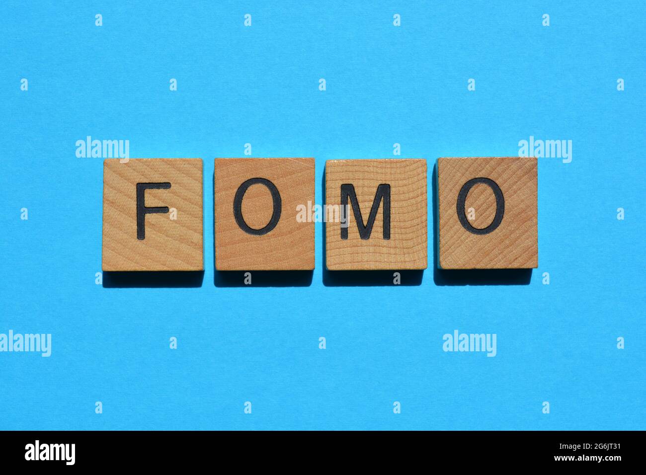 FOMO Akronym, Angst davor, in hölzernen Buchstaben auf blauem Hintergrund isoliert zu fehlen Stockfoto